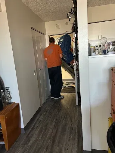 Person in an orange shirt standing in a hallway near coats and a staircase.