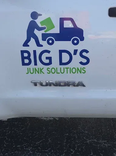 “Big D’s Junk Solutions” logo on a white truck with a blue figure carrying a green bin.