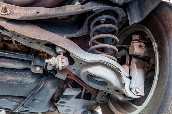 Close-up of a car’s rear suspension, spring, control arm, and brake assembly under the wheel well