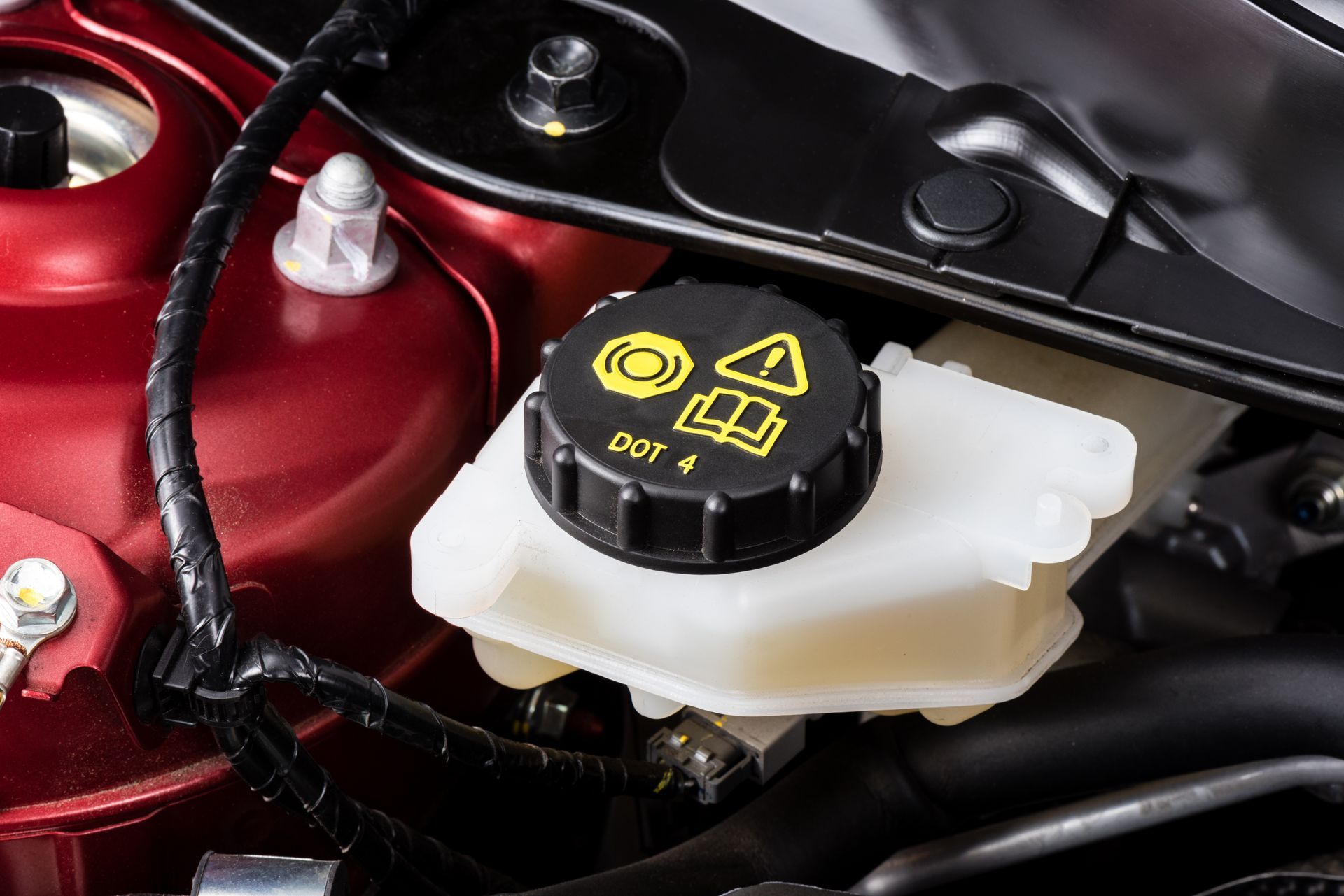 Close-up of a car brake fluid reservoir with a black cap on a red engine bay component
