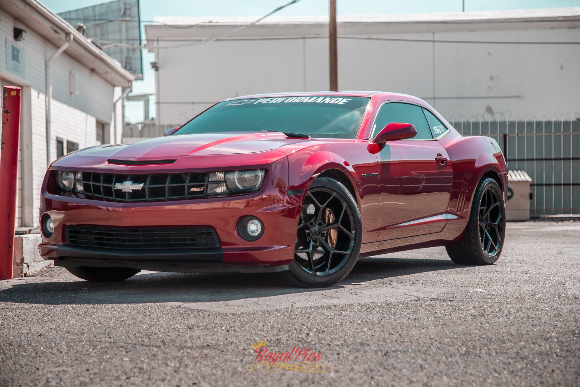Red Chevrolet Camaro parked in an alley, with black wheels and tinted windows.