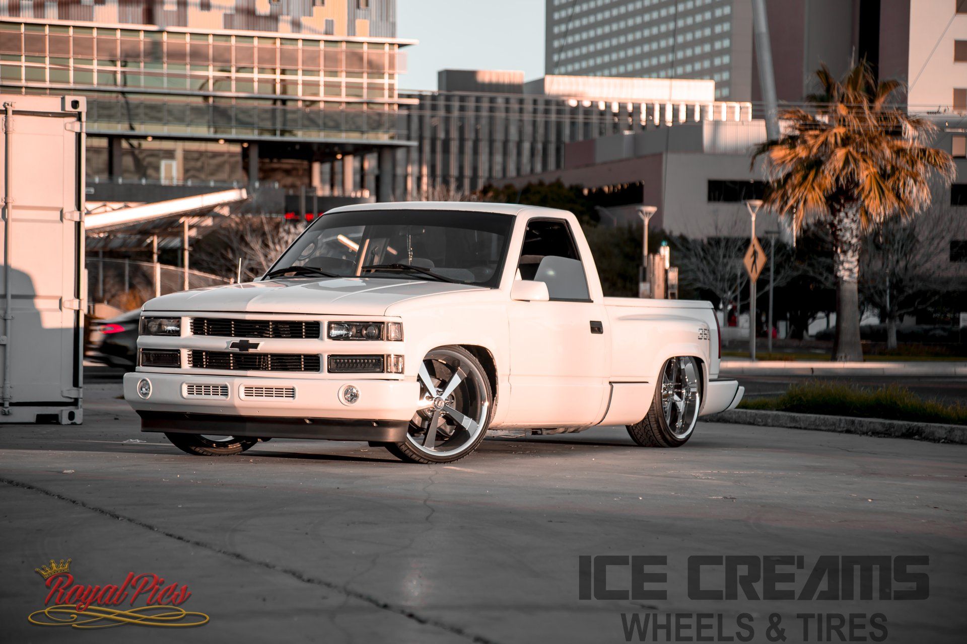 White classic pickup truck parked on a city street at sunset, with palm trees and buildings in the background