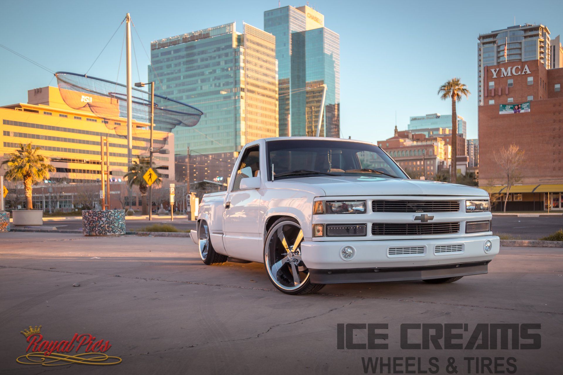 White Chevrolet Silverado parked in a city street at sunset, with downtown buildings in the background.