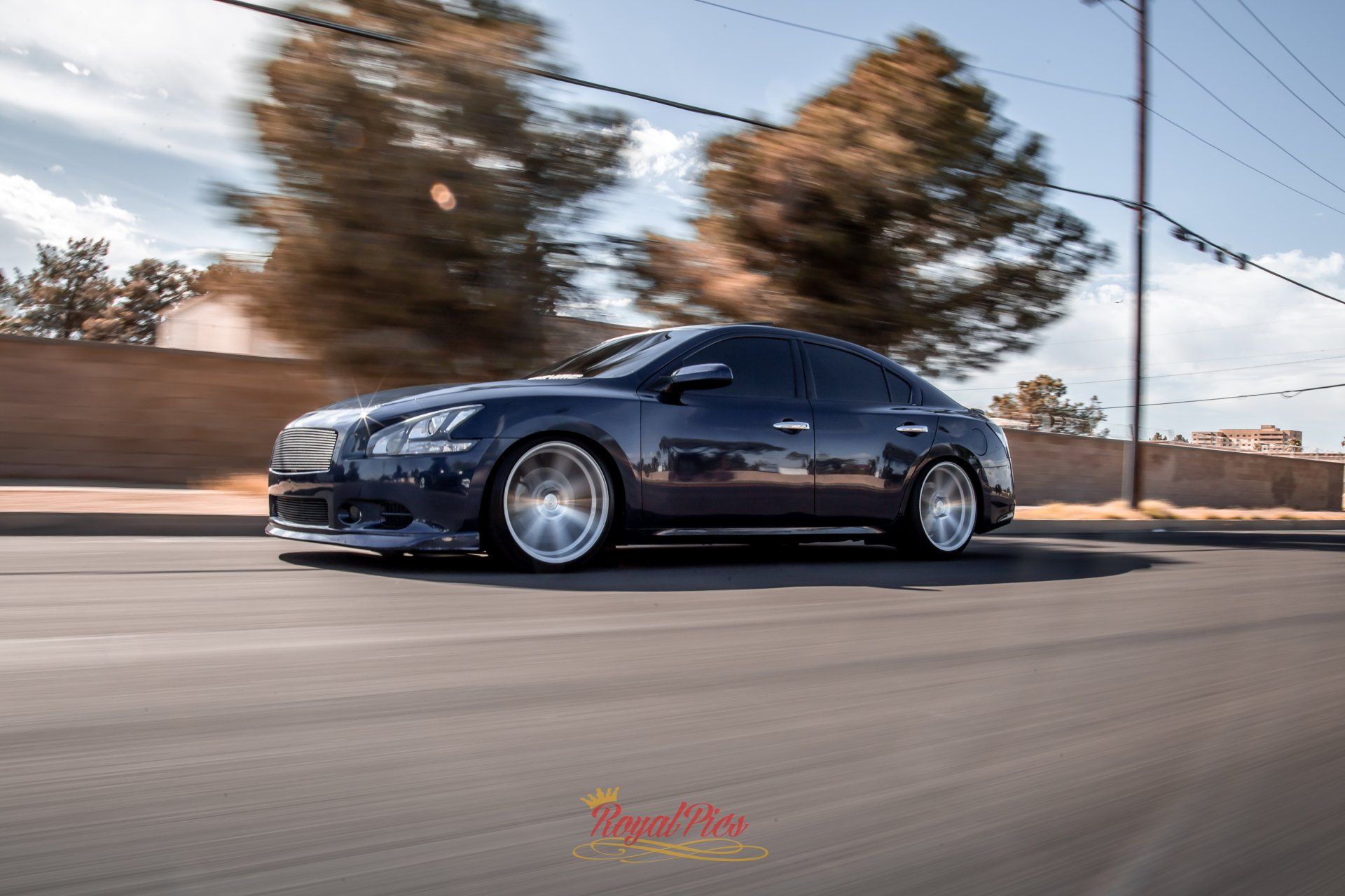 Dark blue sedan driving fast on a road with motion blur and trees in the background