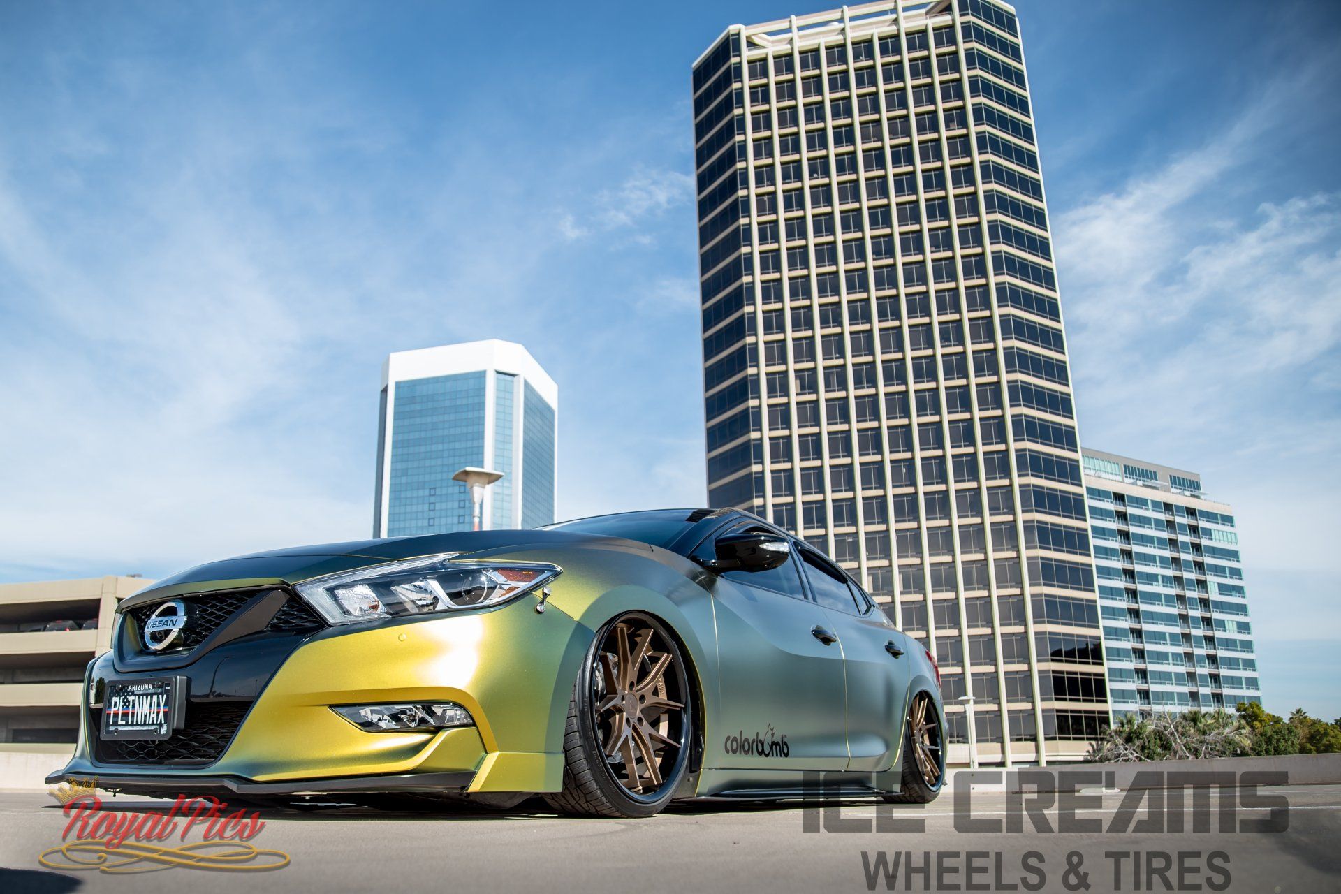 Modified silver and gold sports car parked low in front of city skyscrapers under a blue sky