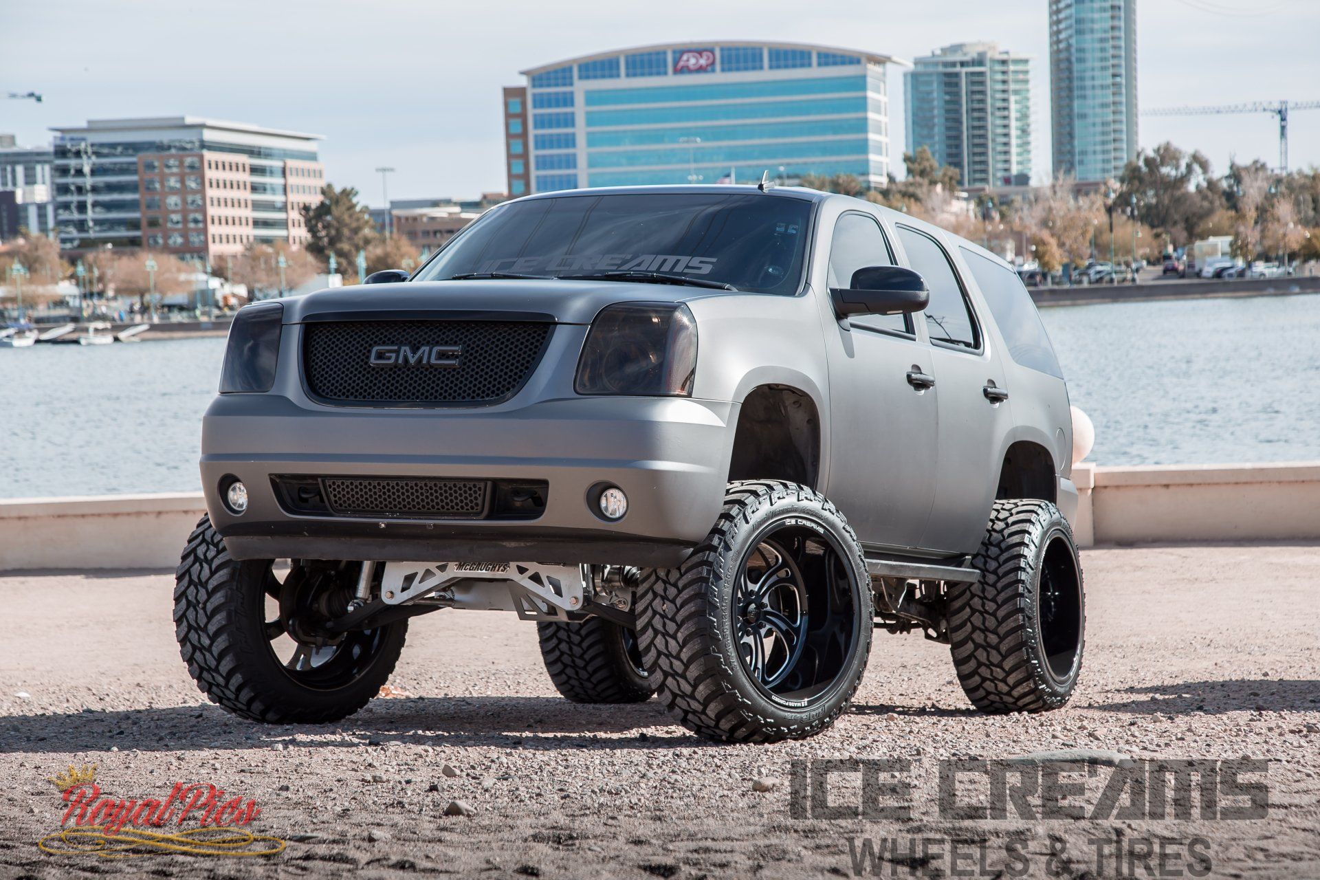 Lifted gray GMC pickup truck parked by a waterfront city skyline