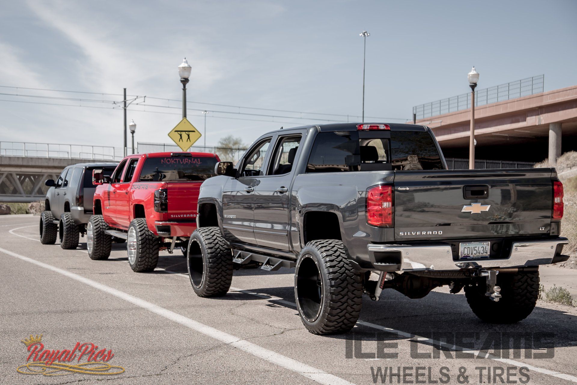 Line of lifted pickup trucks parked on a highway shoulder beside an overpass