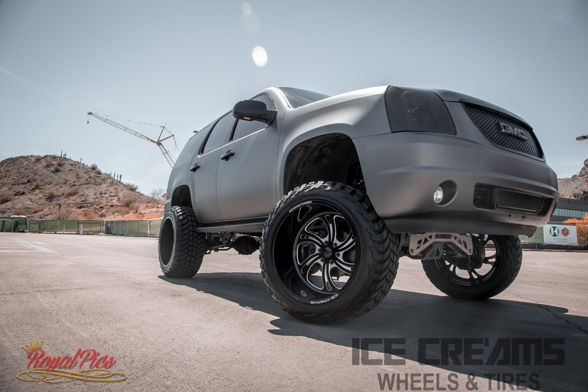 Lifted gray pickup truck on a road with desert hills and construction crane in the background.