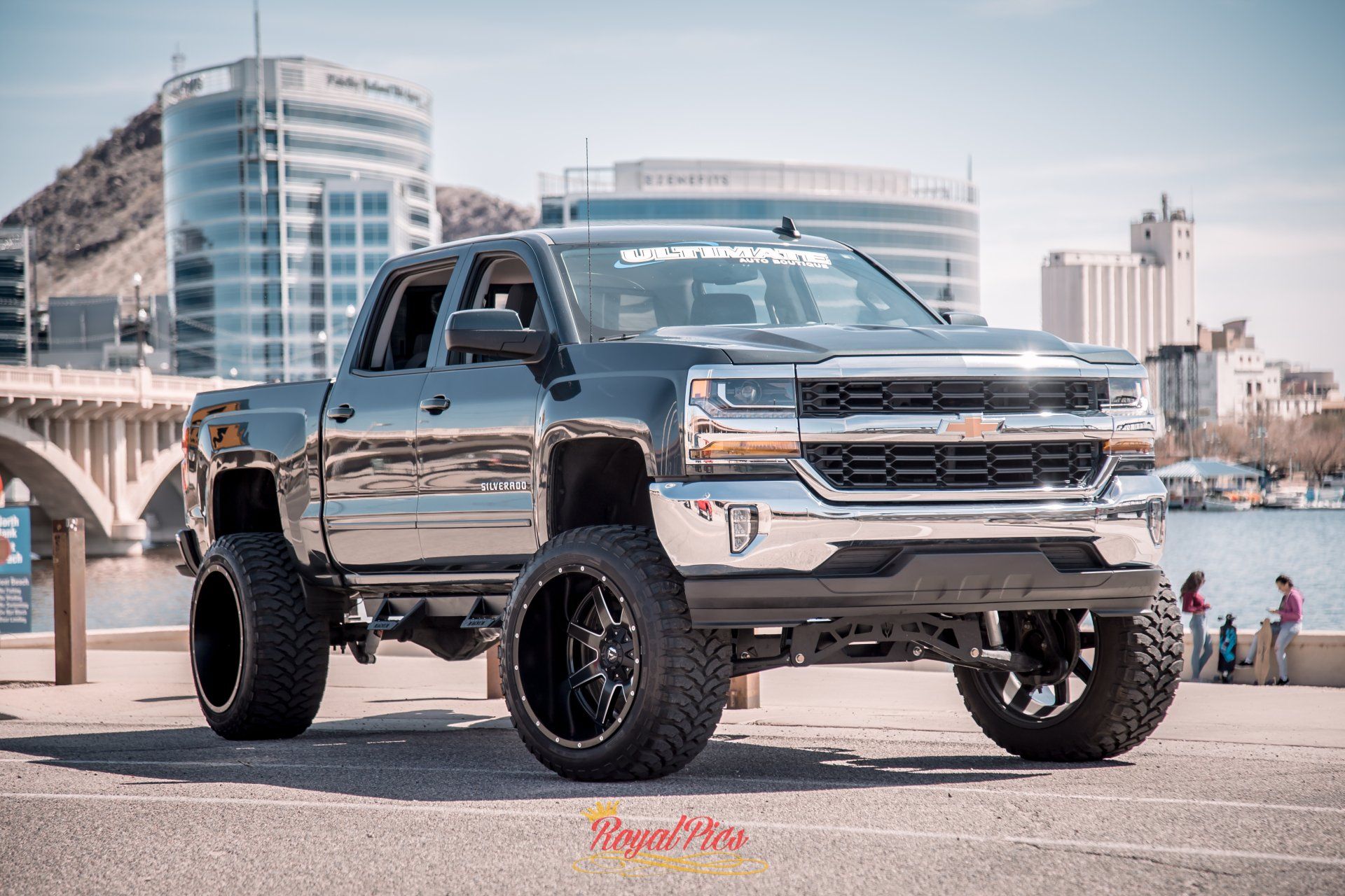 Lifted black pickup truck parked on a waterfront street with city buildings in the background