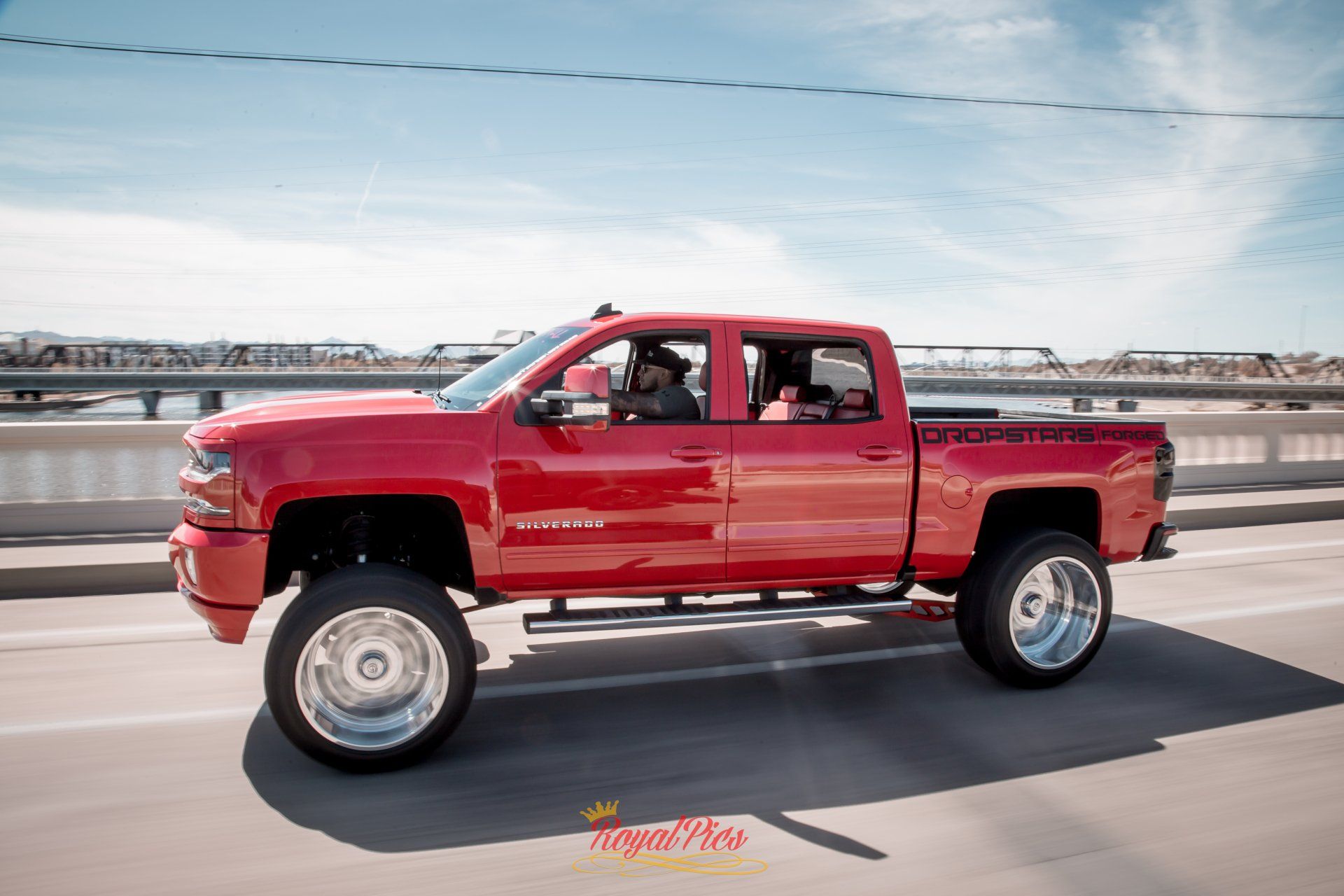Red lifted pickup truck driving on a bridge with water in the background