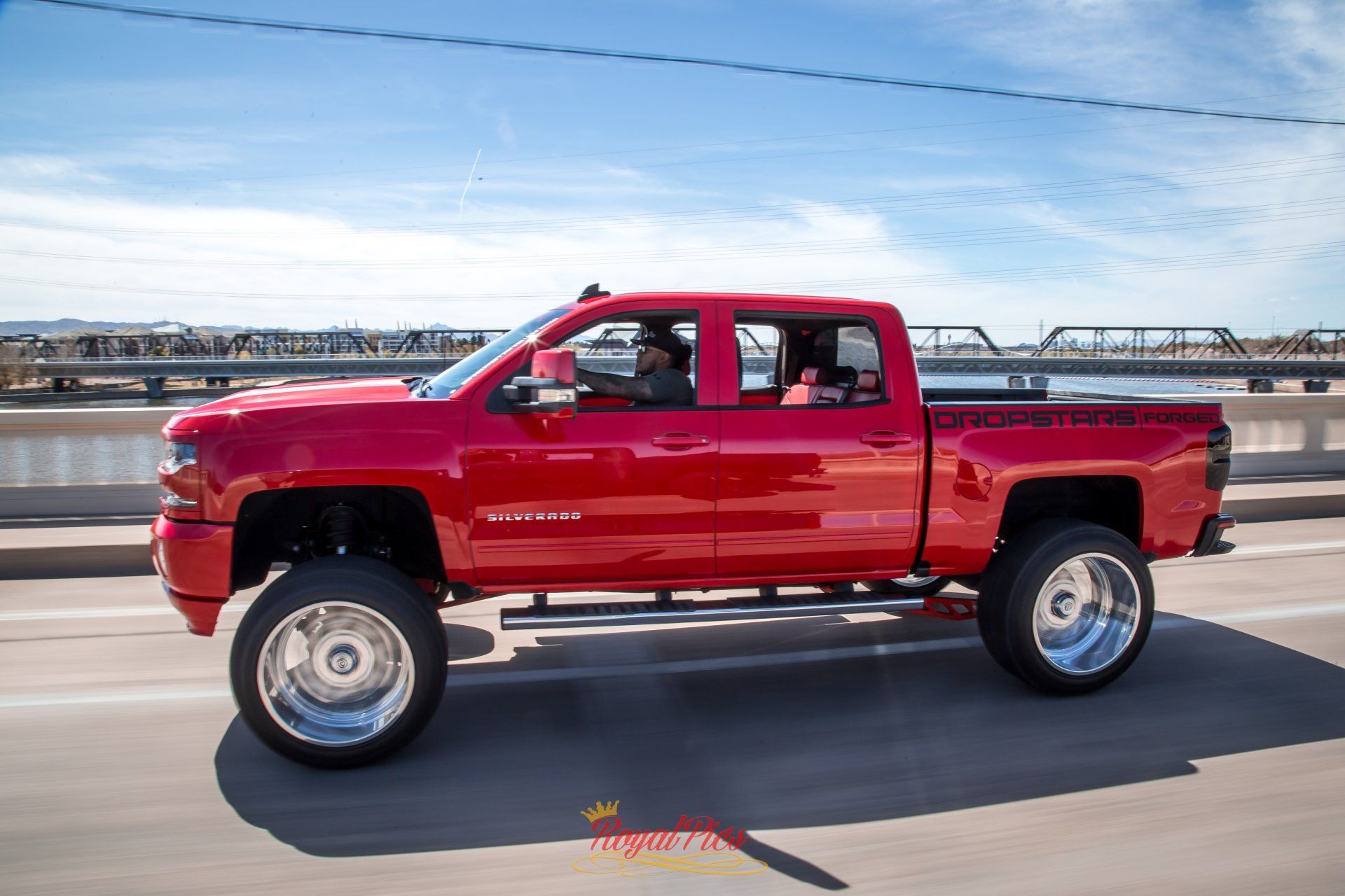 Red lifted pickup truck driving on a bridge under a blue sky