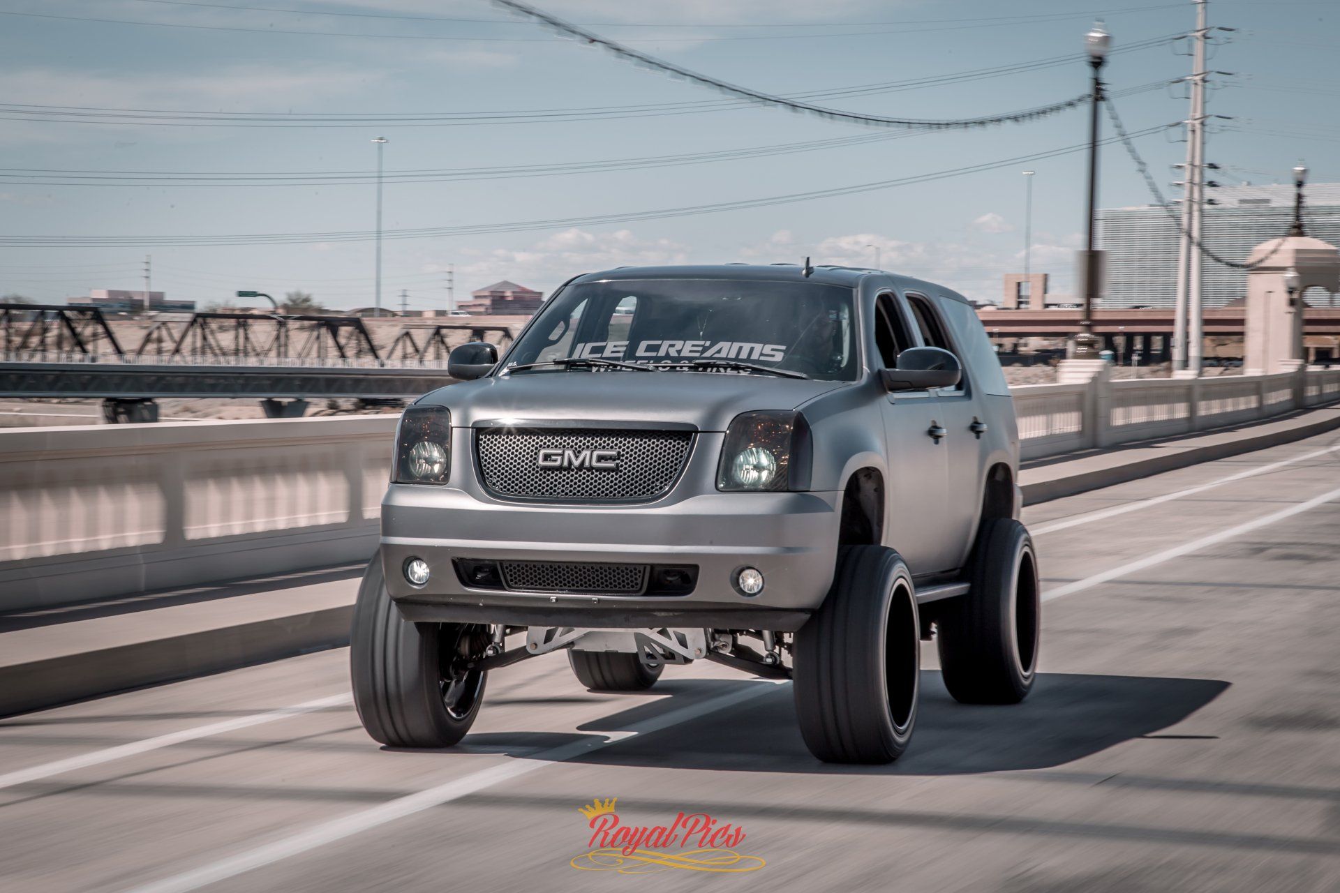 Gray GMC pickup truck driving on a bridge, with a waterfront city skyline in the background