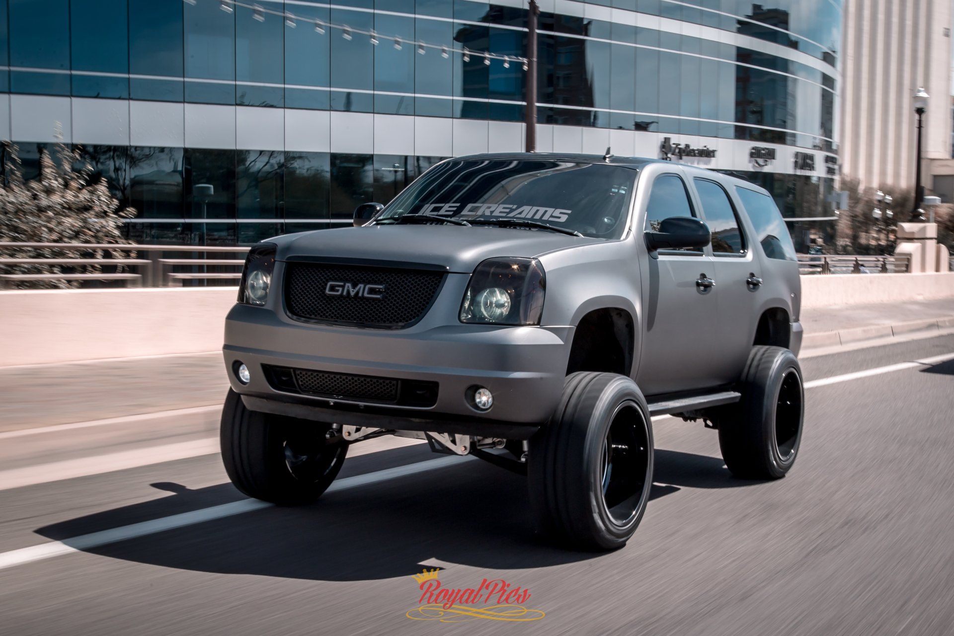 Lifted gray GMC SUV driving on a city street beside modern glass buildings