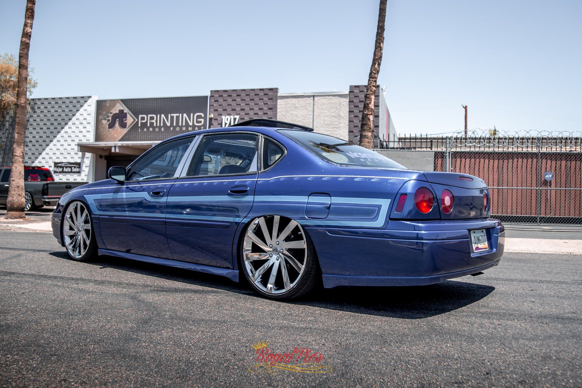 Blue lowered sedan parked outside a printing shop on a sunny street