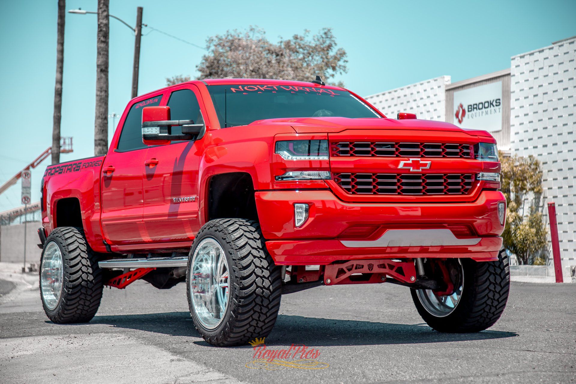 Lifted red pickup truck parked outdoors near a dealership building.