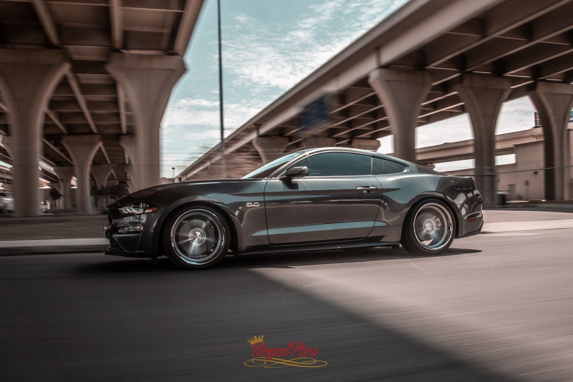 Black sports car driving under an elevated highway in an urban setting