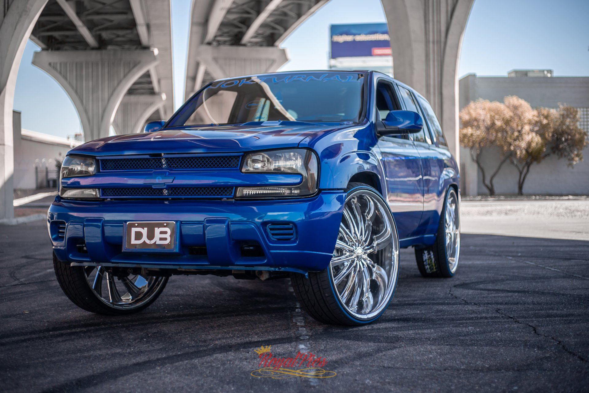 Blue SUV with large chrome wheels parked under an overpass, front view