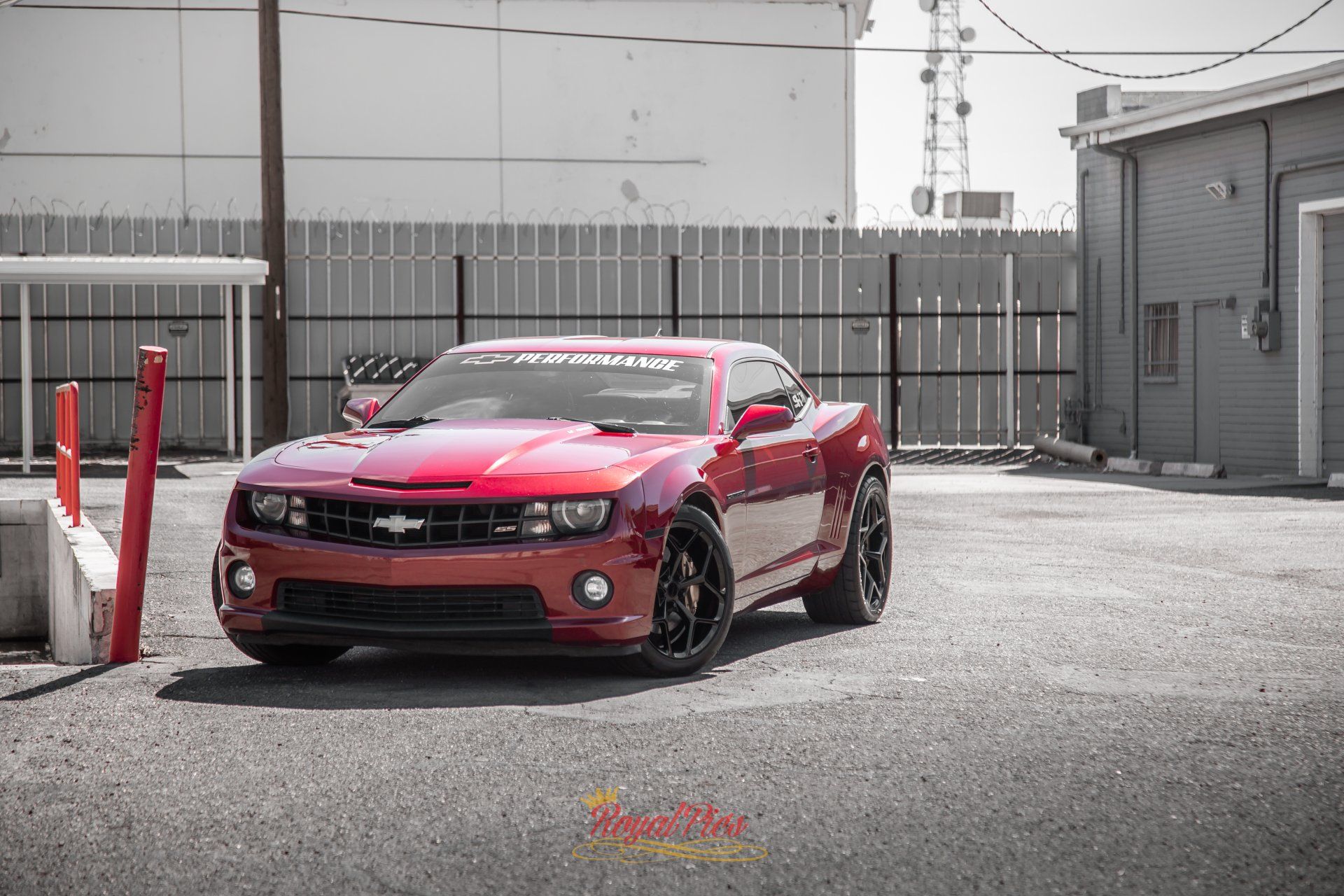 Red sports car parked in an industrial lot beside a building and fence