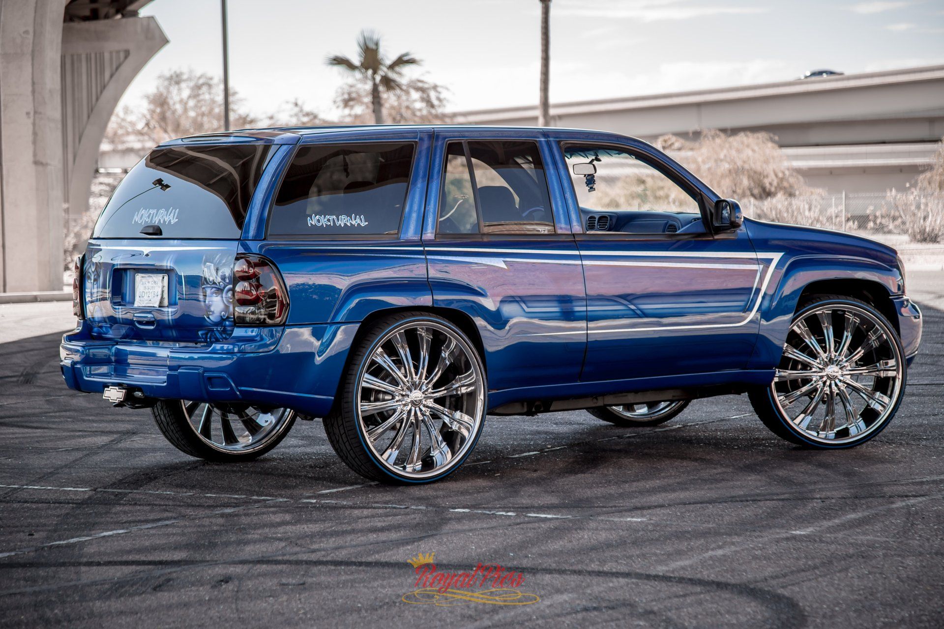 Blue lifted SUV with chrome rims parked outdoors near an overpass