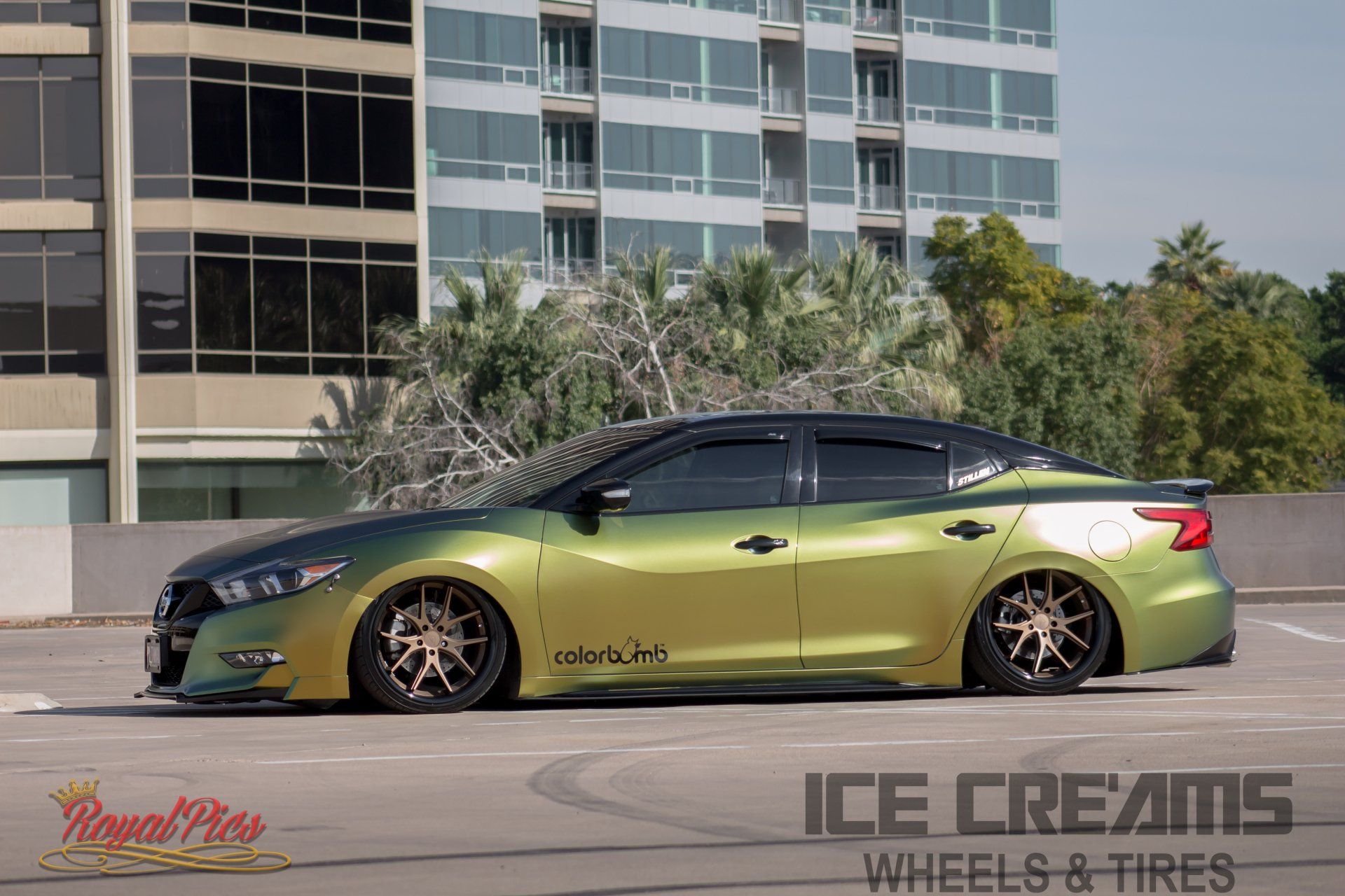 Custom green lowrider sedan parked outdoors in front of a building, with gold wheels and tinted windows