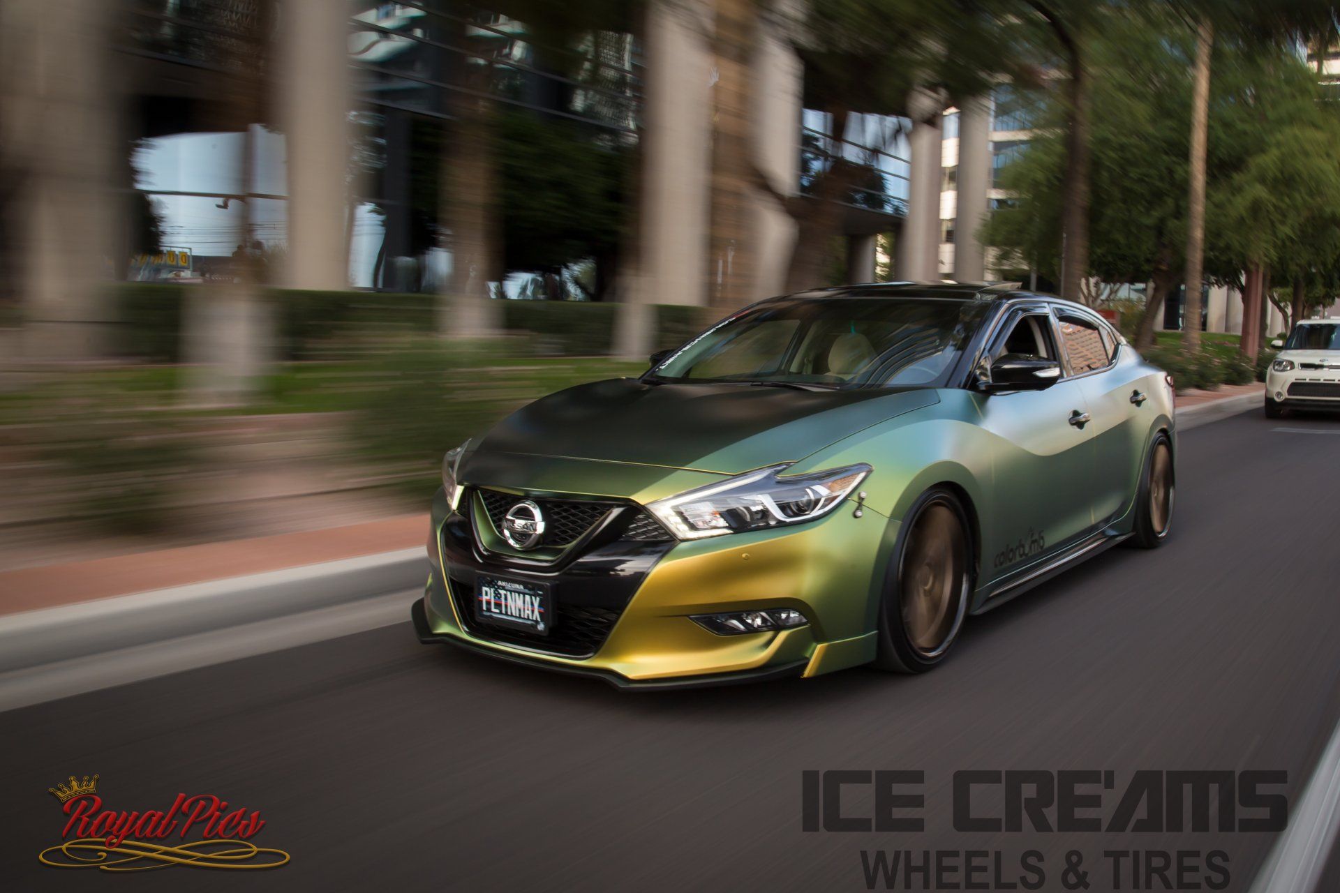 Green Nissan sedan driving on a city street, with motion blur and custom wheels