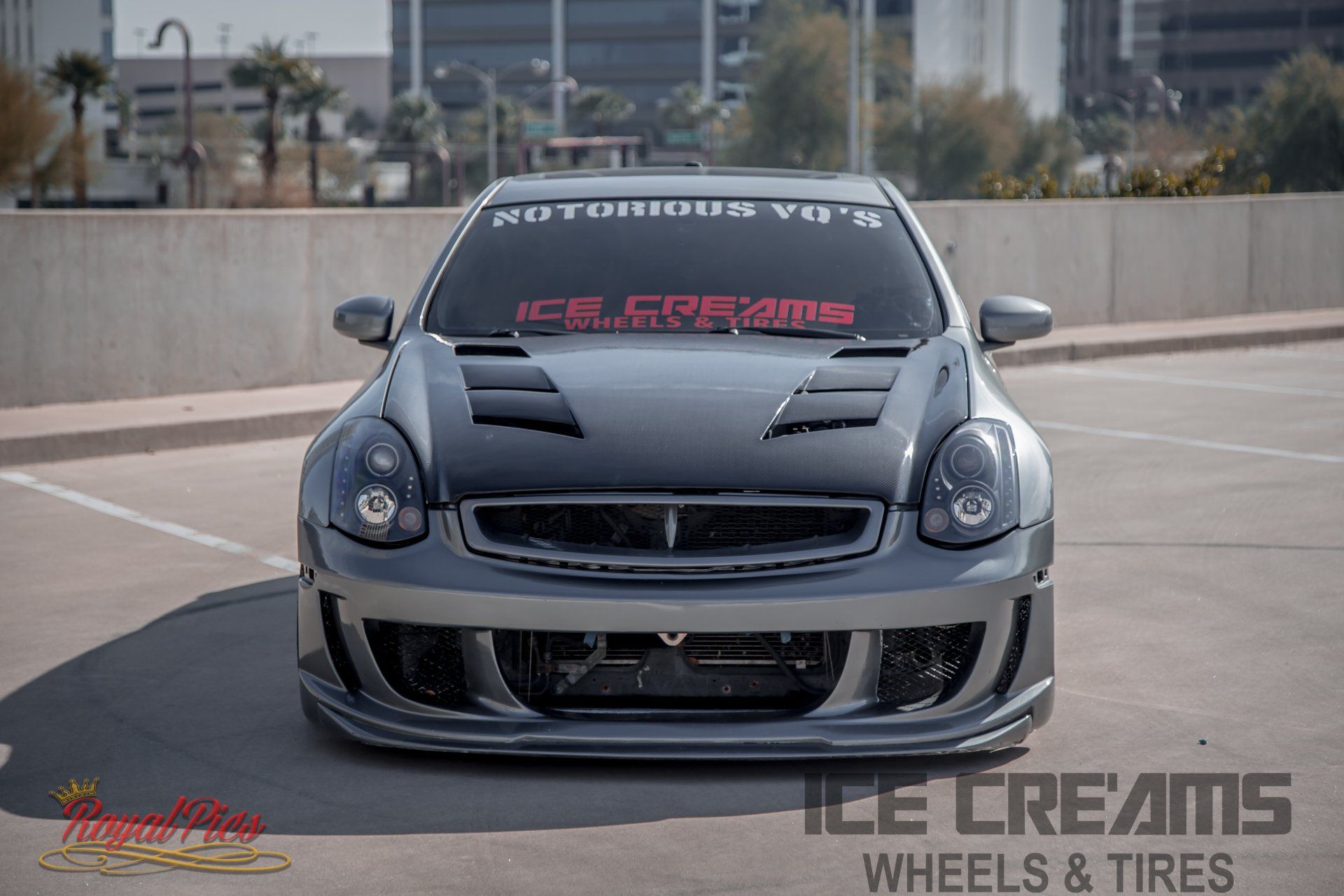 Gray modified sports car front view in a parking lot with “LE CREAMS” windshield banner and hood decal