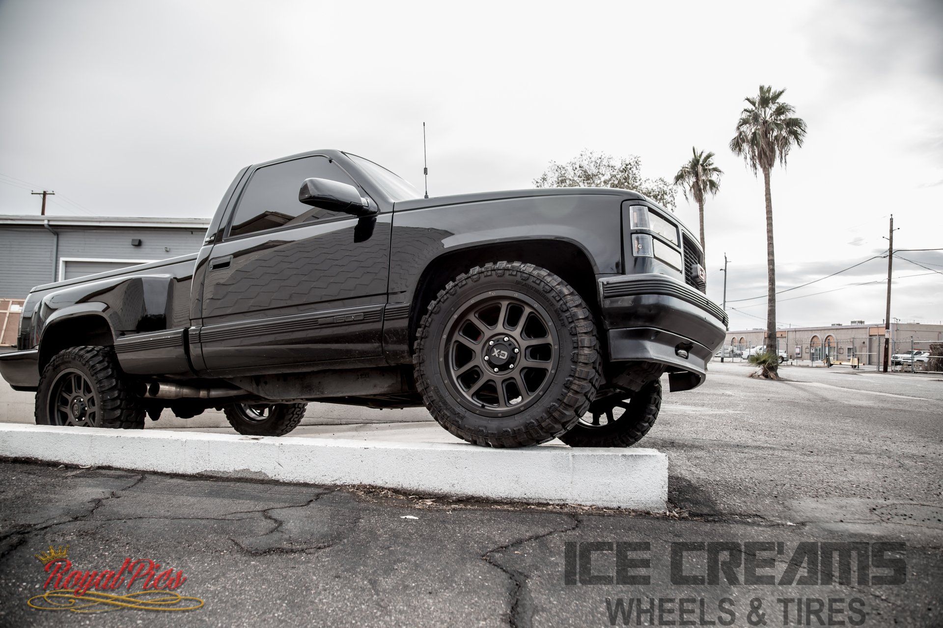 Black lifted pickup truck parked on a curb outside an ice cream wheel and tire shop