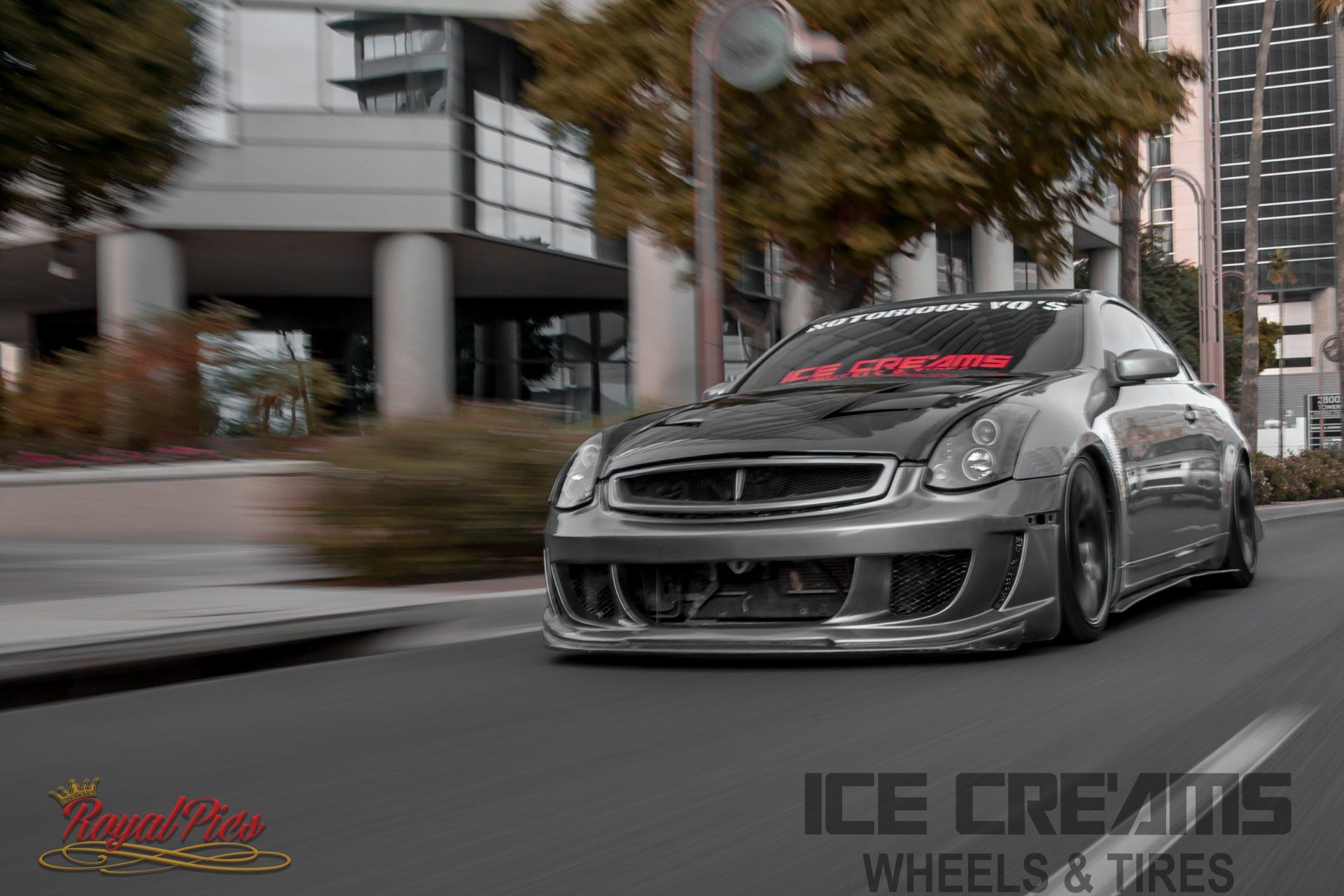 Lowered gray sports car speeding through a city street with motion blur and wheel shop branding.