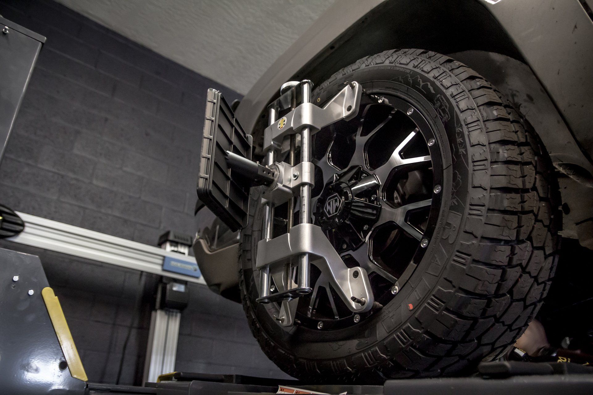 Black off-road tire mounted on a wheel alignment machine in a garage