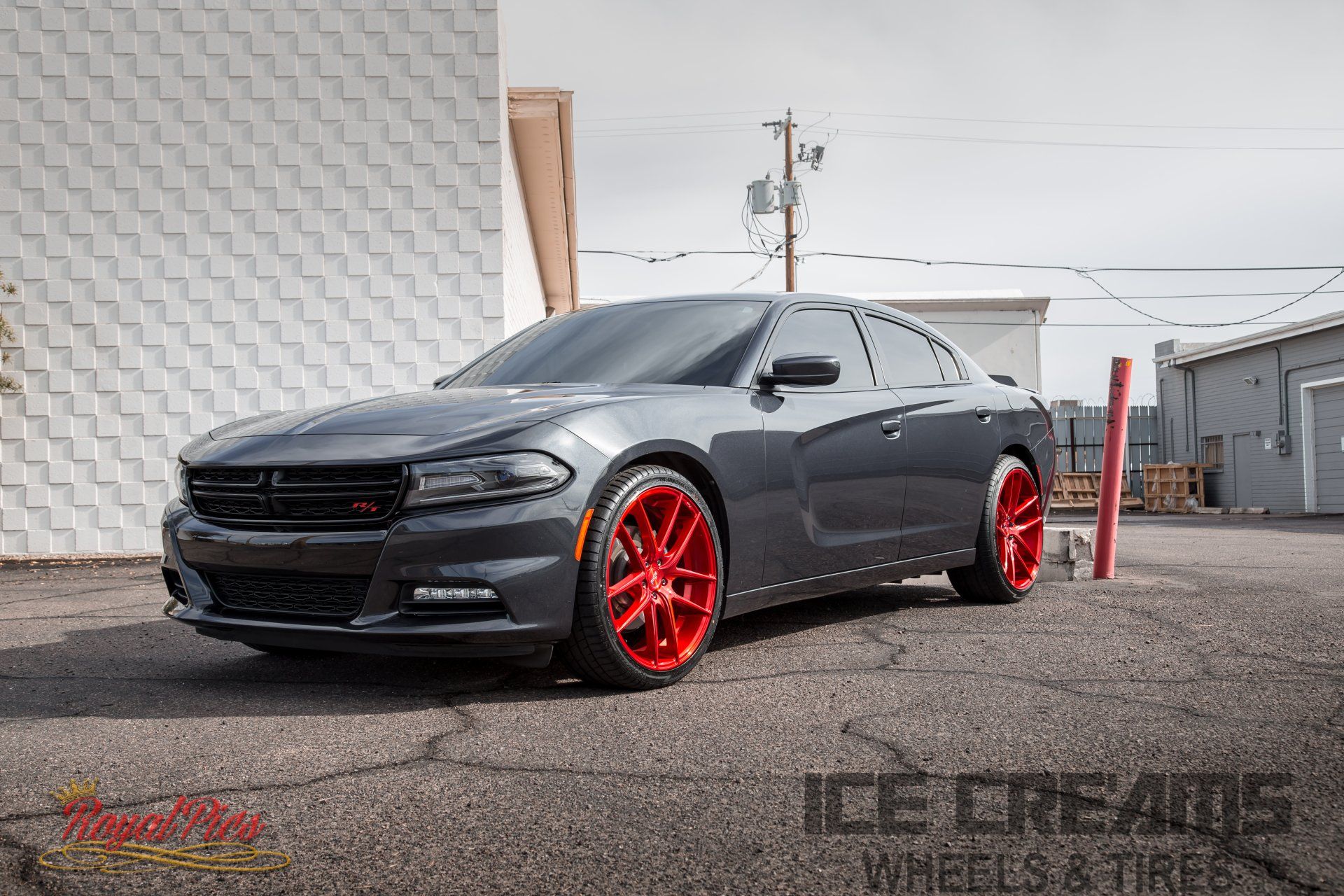 Dark gray Dodge Charger with bright red rims parked outdoors by a building