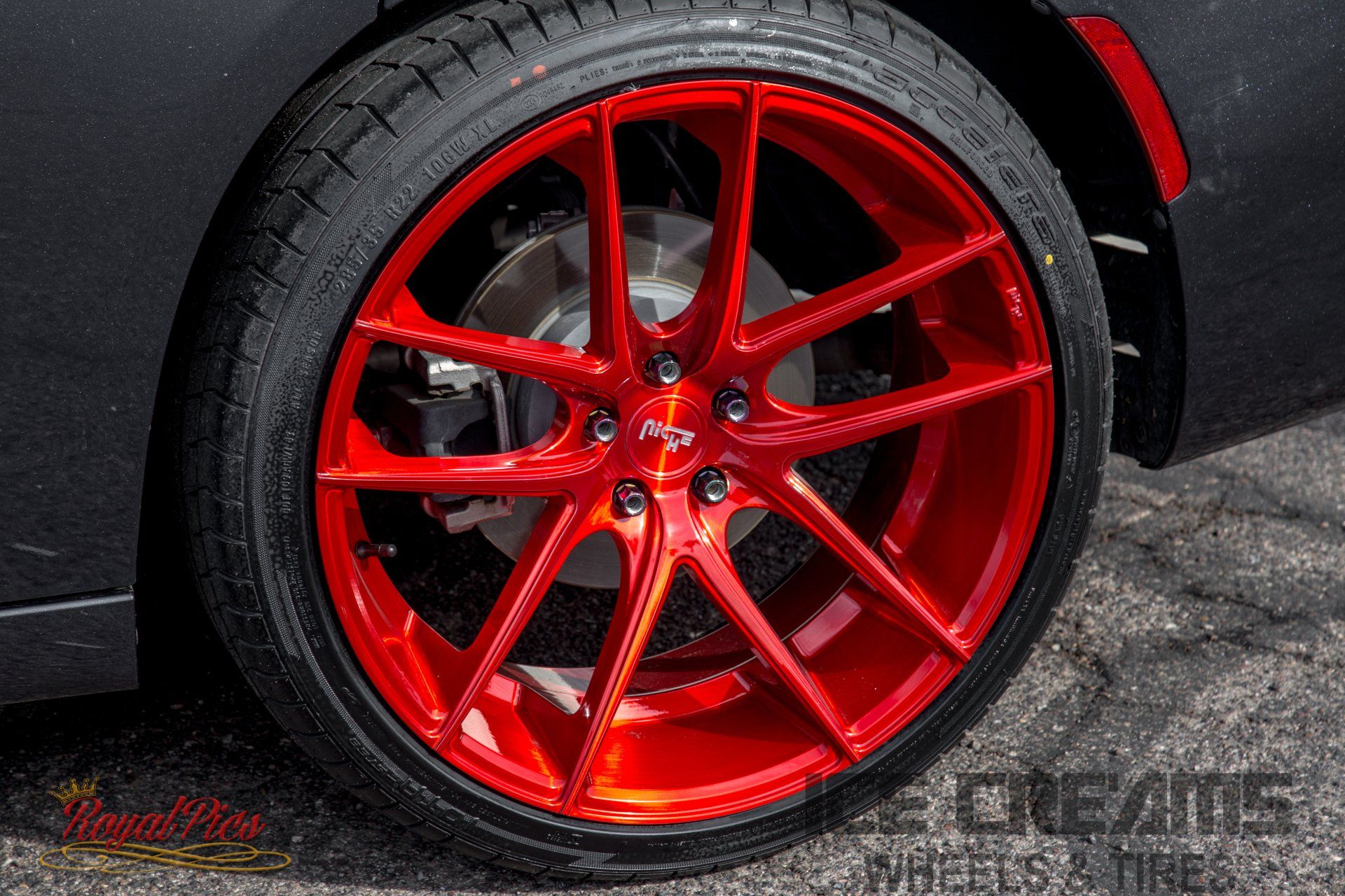Close-up of a red sports car wheel with glossy red rim and black tire on dark pavement