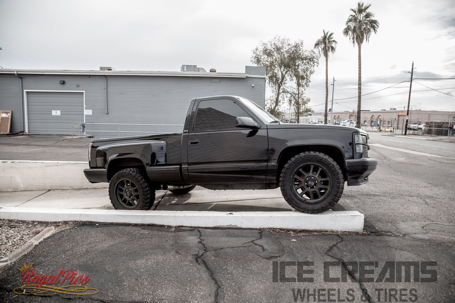 Black lifted pickup truck parked beside a warehouse on a wet street.