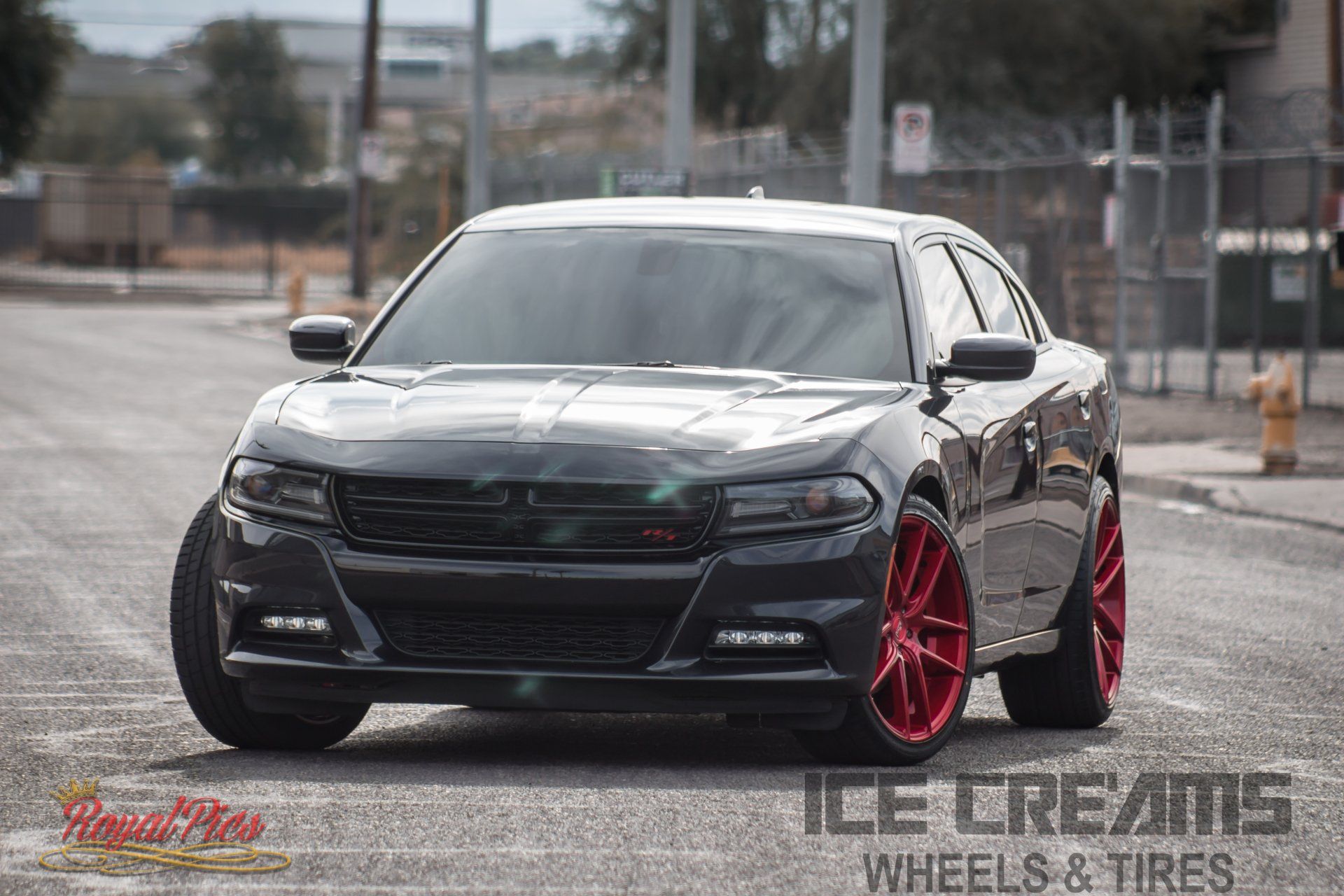 Black Dodge Charger with bright red rims parked on a wet street, front view