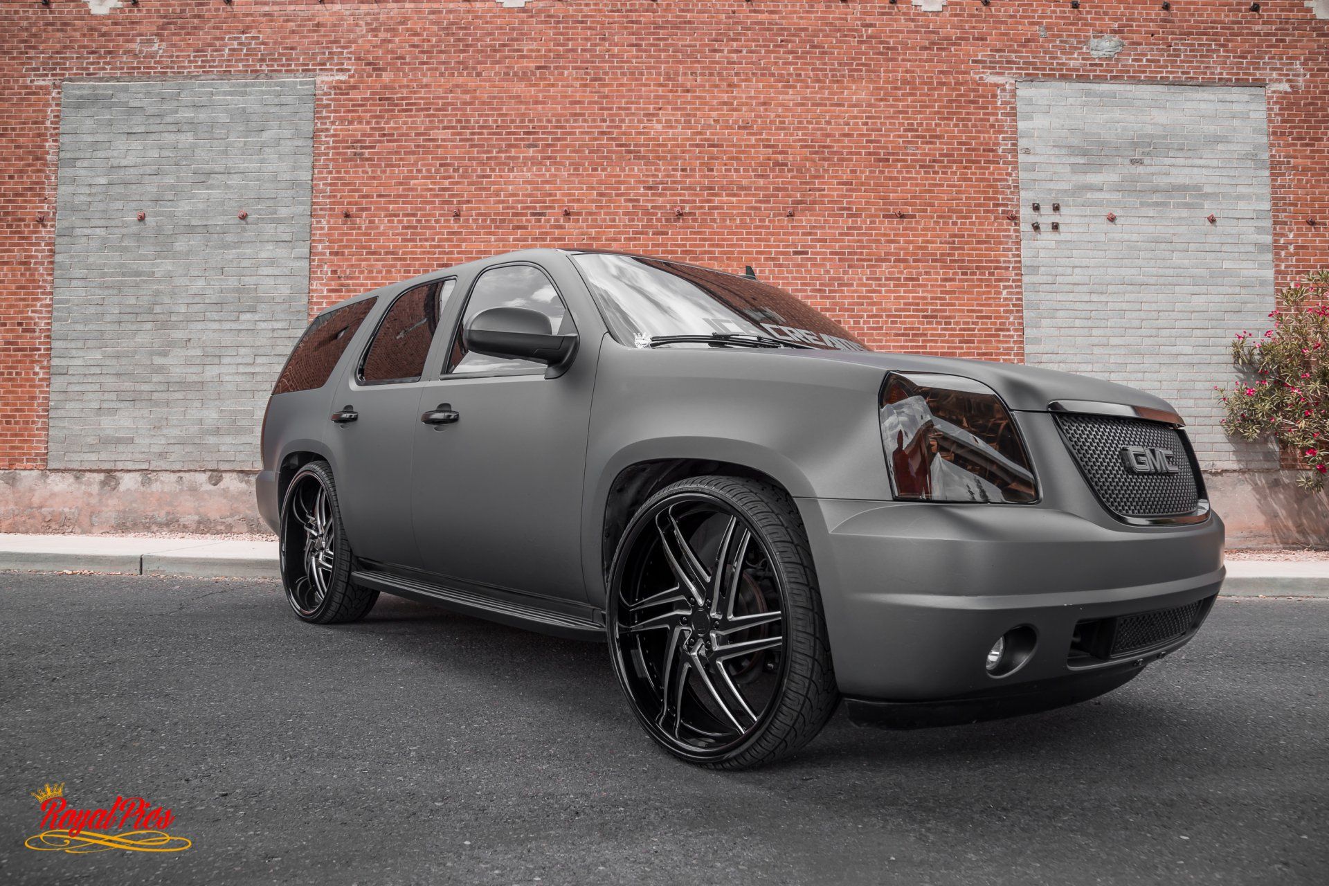 Matte gray SUV parked beside a brick wall with black custom rims