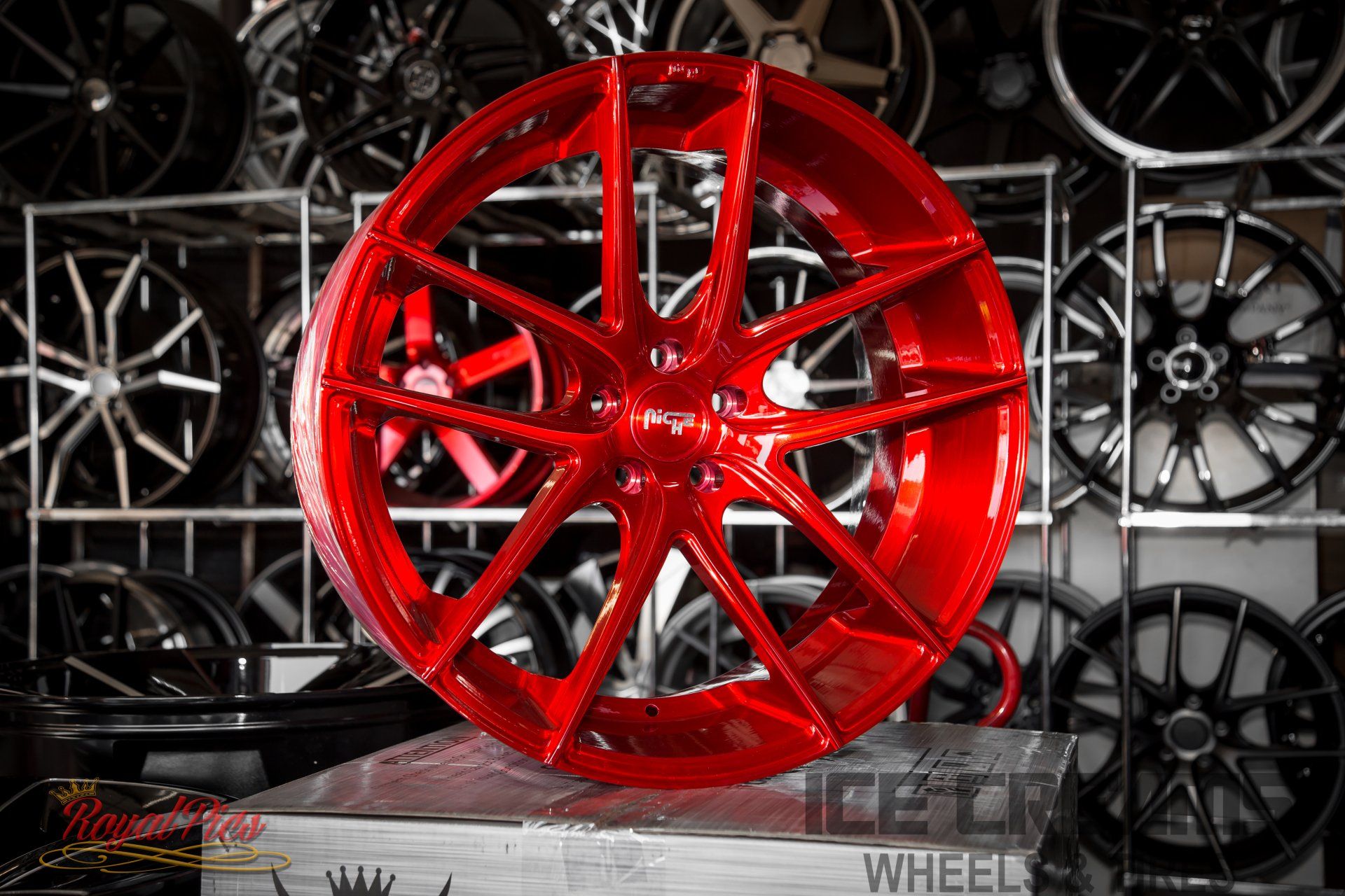 Bright red custom alloy wheel displayed on a stand, with black and silver rims in the background