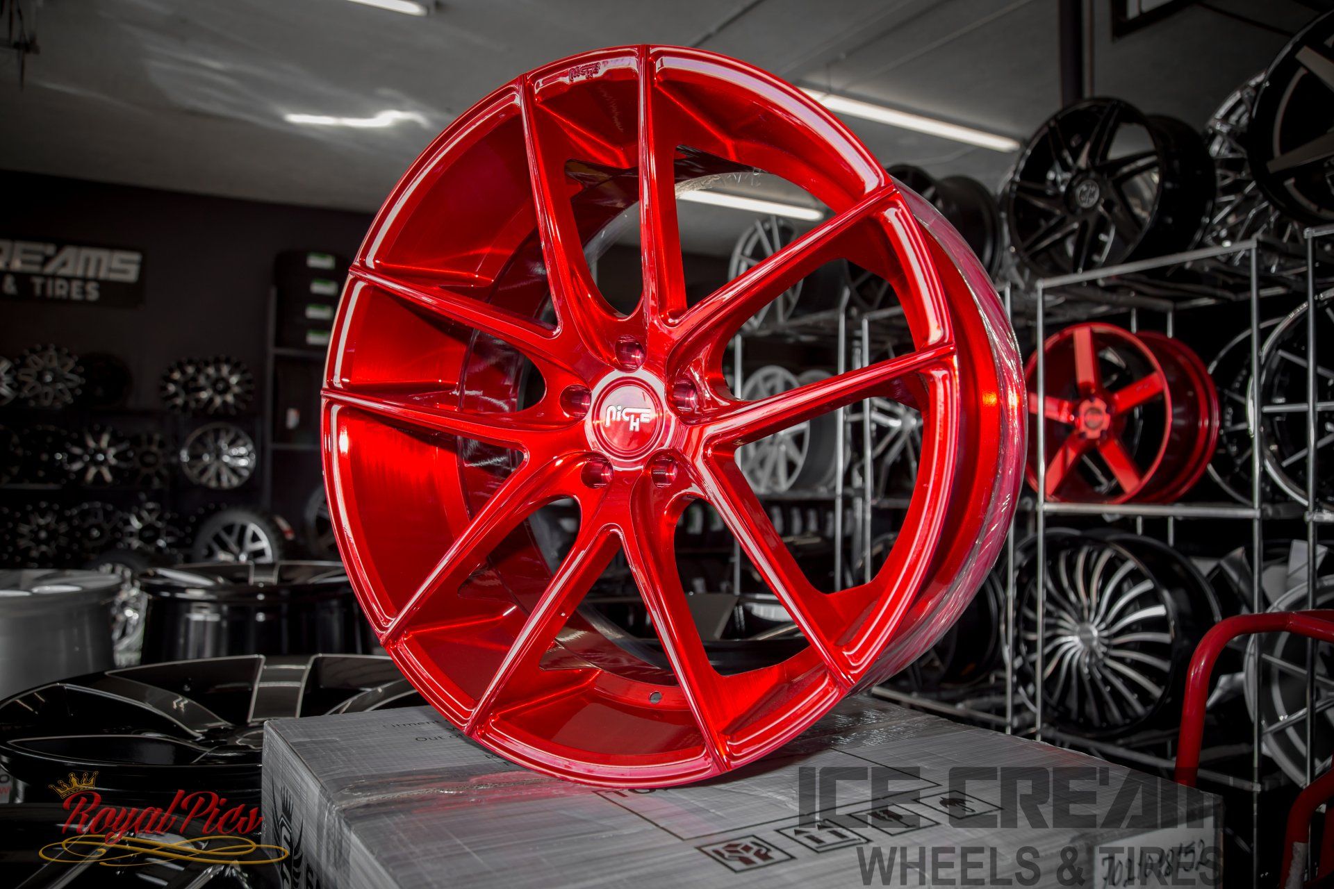 Bright red custom alloy wheel displayed in a tire shop, with black rims in the background