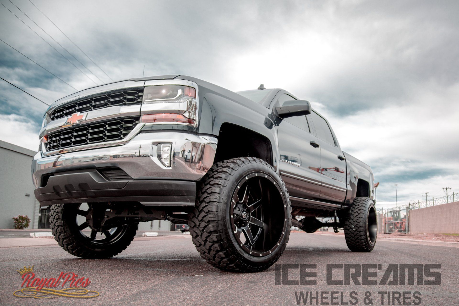 Lifted gray pickup truck with oversized black wheels in a parking lot under cloudy skies