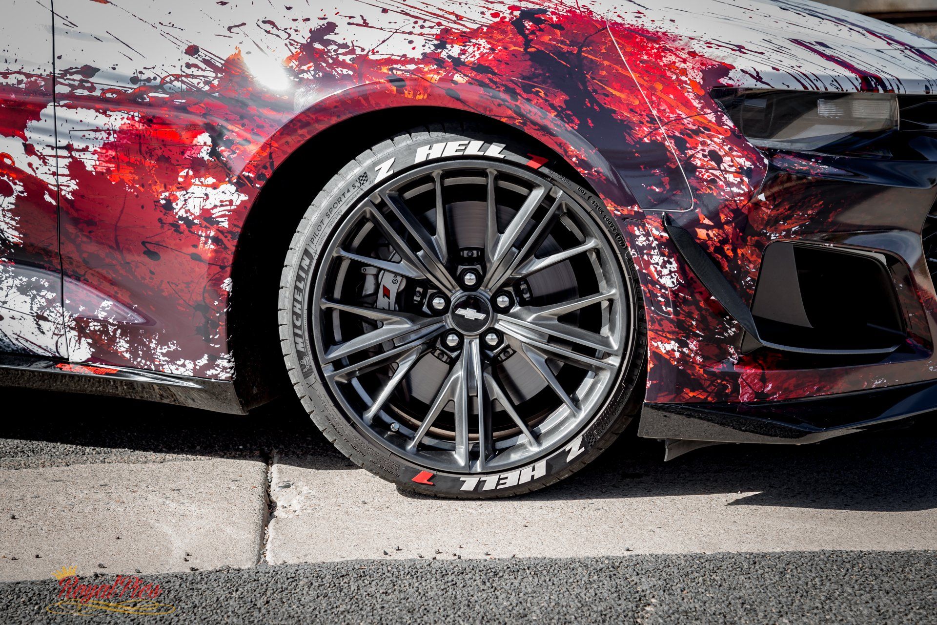 Red sports car with black wheel and red-white paint splatter, parked by a curb.