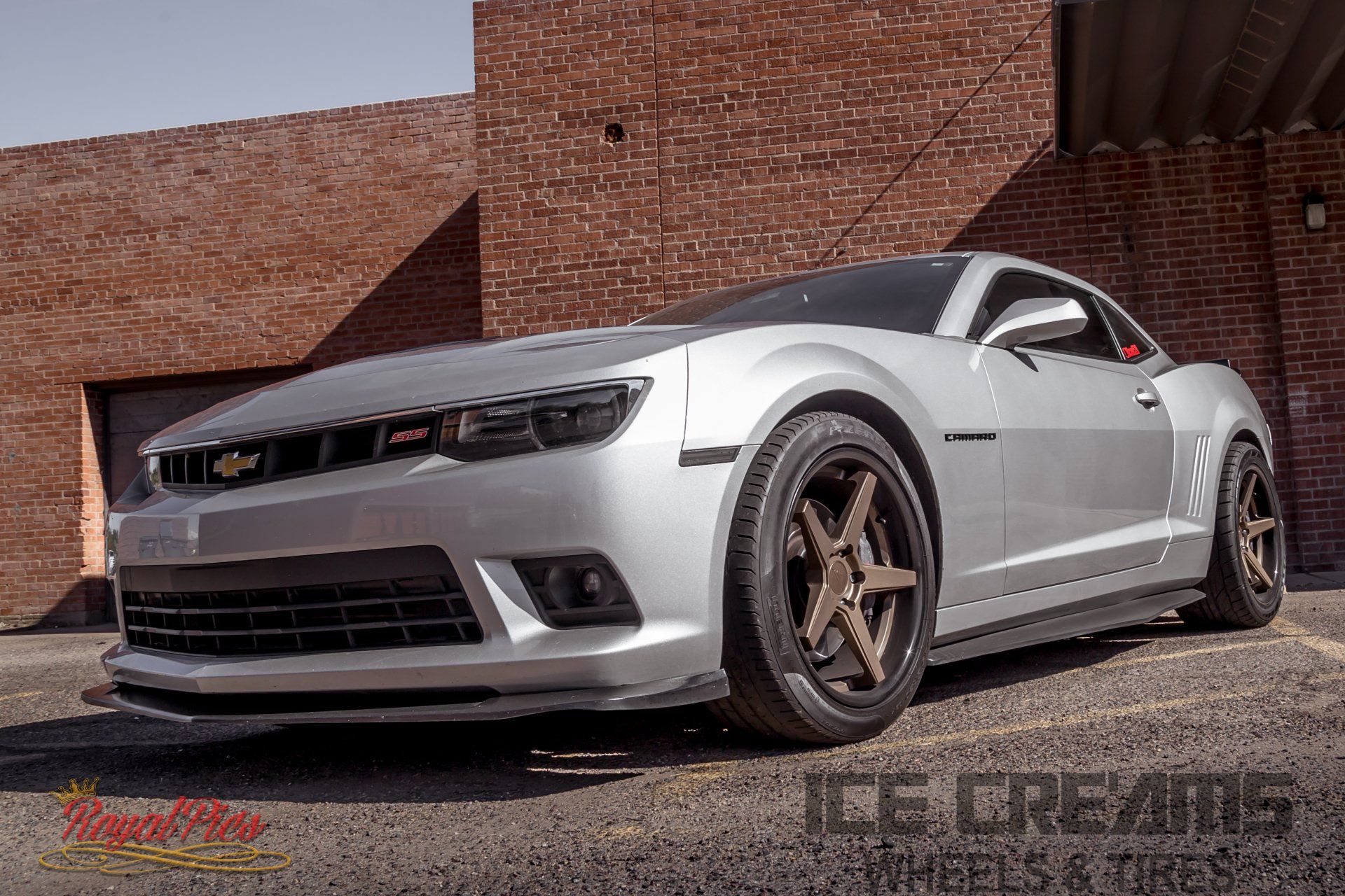 Silver sports car parked beside a brick building, low-angle front view with bronze wheels.