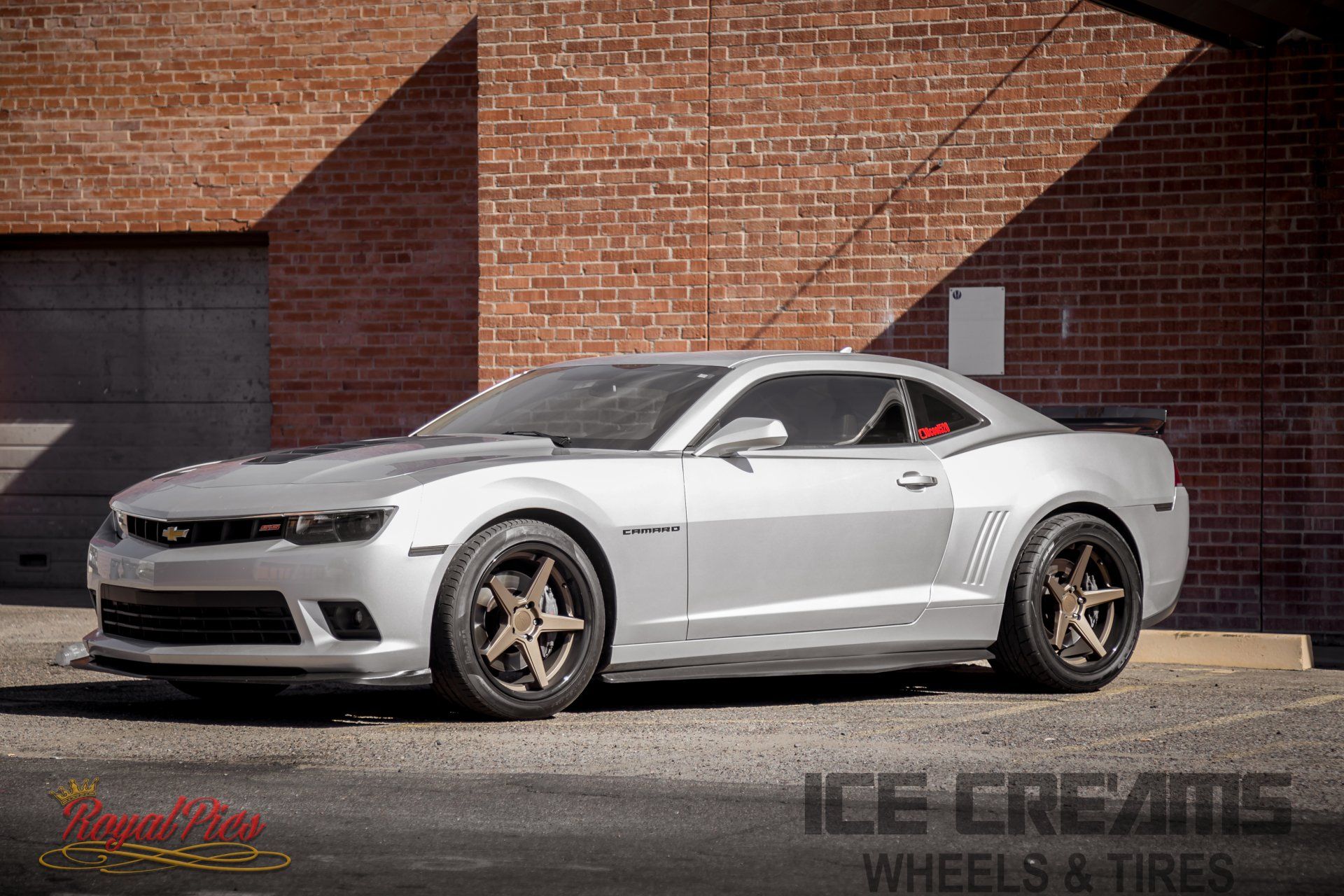 Silver Chevrolet Camaro parked by a brick wall, lowered with bronze wheels.
