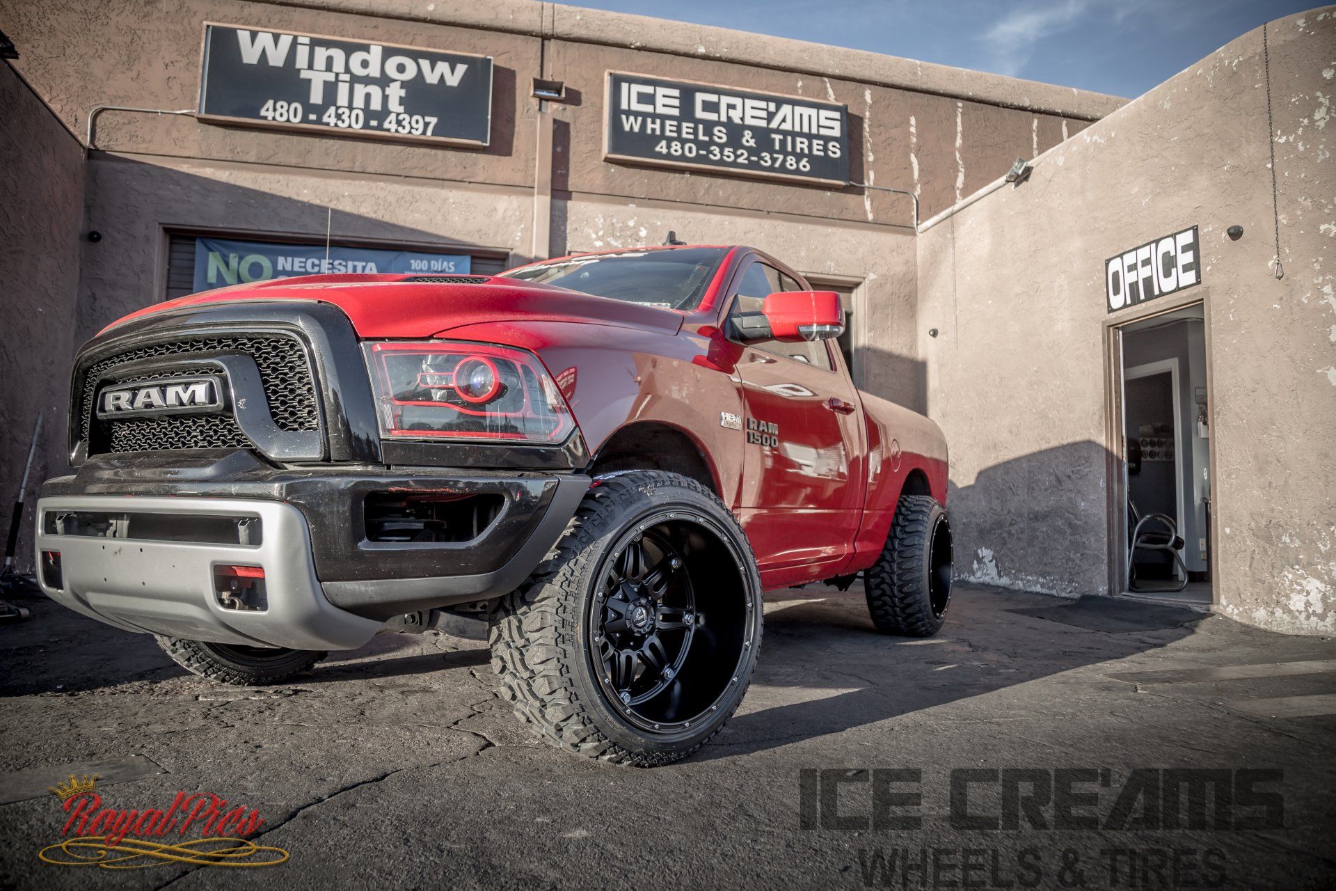 Red lifted RAM pickup truck parked outside an Ice Cream Wheels & Tires shop.