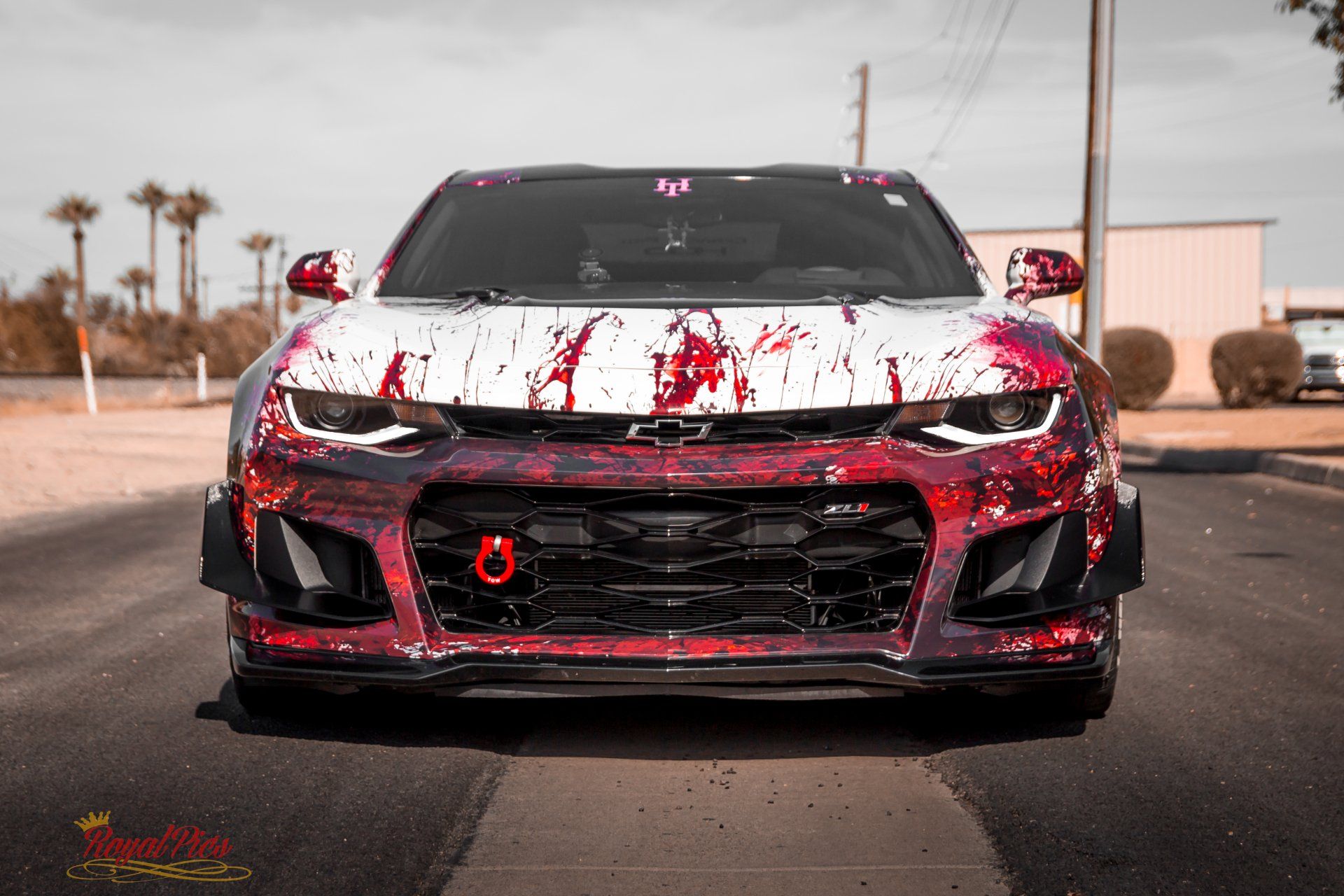 Front view of a red sports car with white paint splatters on an open road.