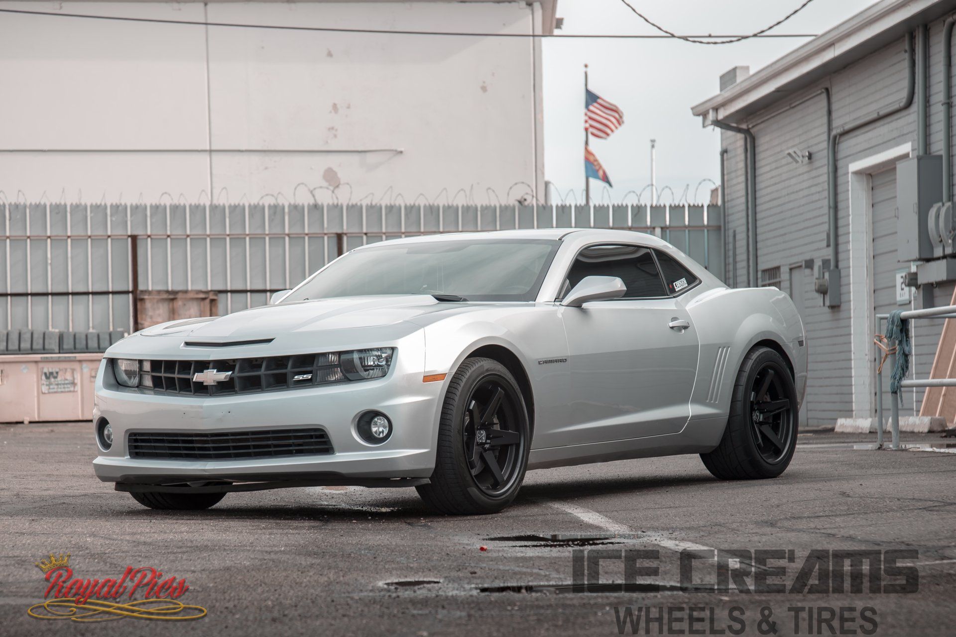Silver Chevrolet Camaro parked in an industrial lot with black wheels and a rear spoiler