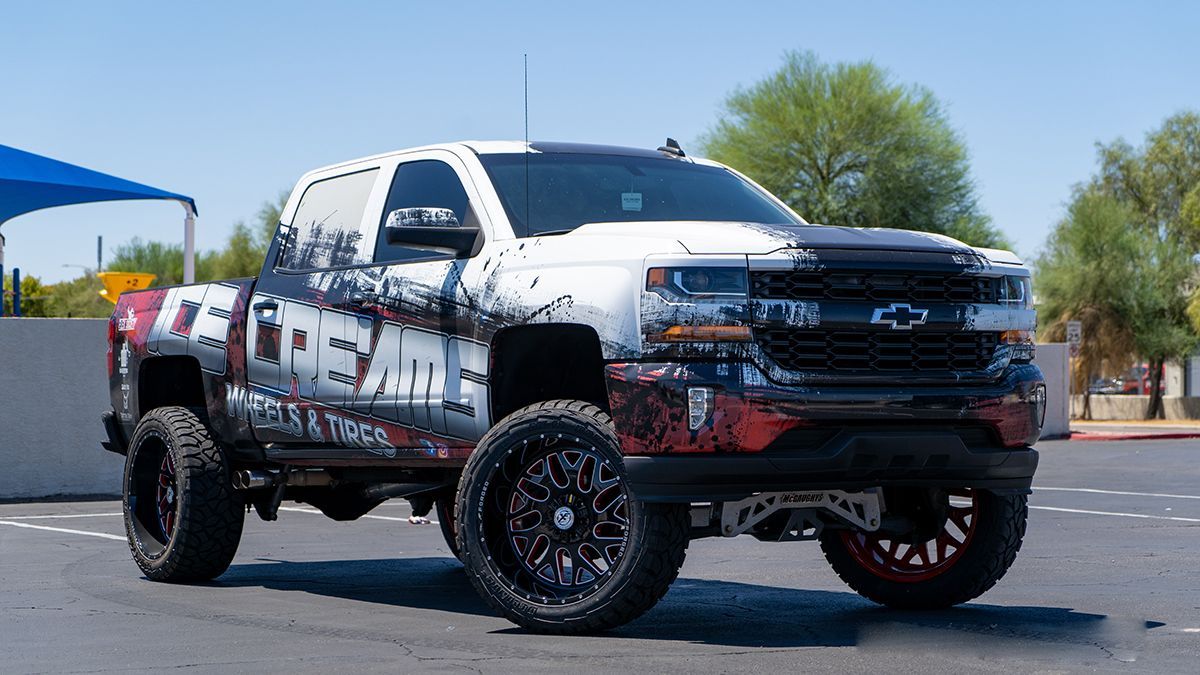 Lifted white and black pickup truck with off-road tires parked outdoors on a sunny day