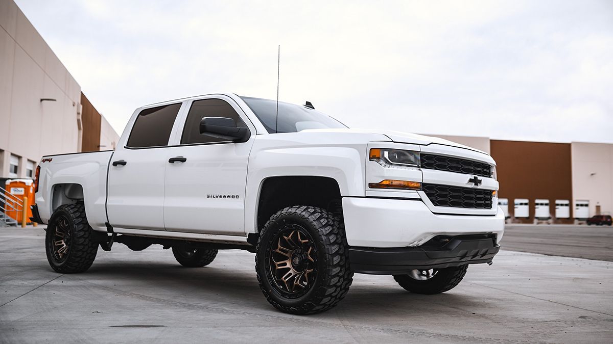 White lifted Chevrolet pickup truck parked on pavement, front three-quarter view with black wheels