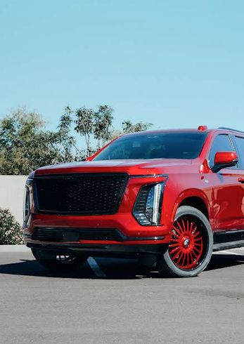 Red custom SUV with black grille and red rims parked on a road under a clear blue sky