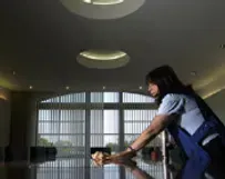 Woman wiping a table in a bright lobby with large windows and round ceiling lights