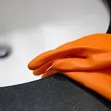 Orange gloved hand holding a black fabric edge against a white background