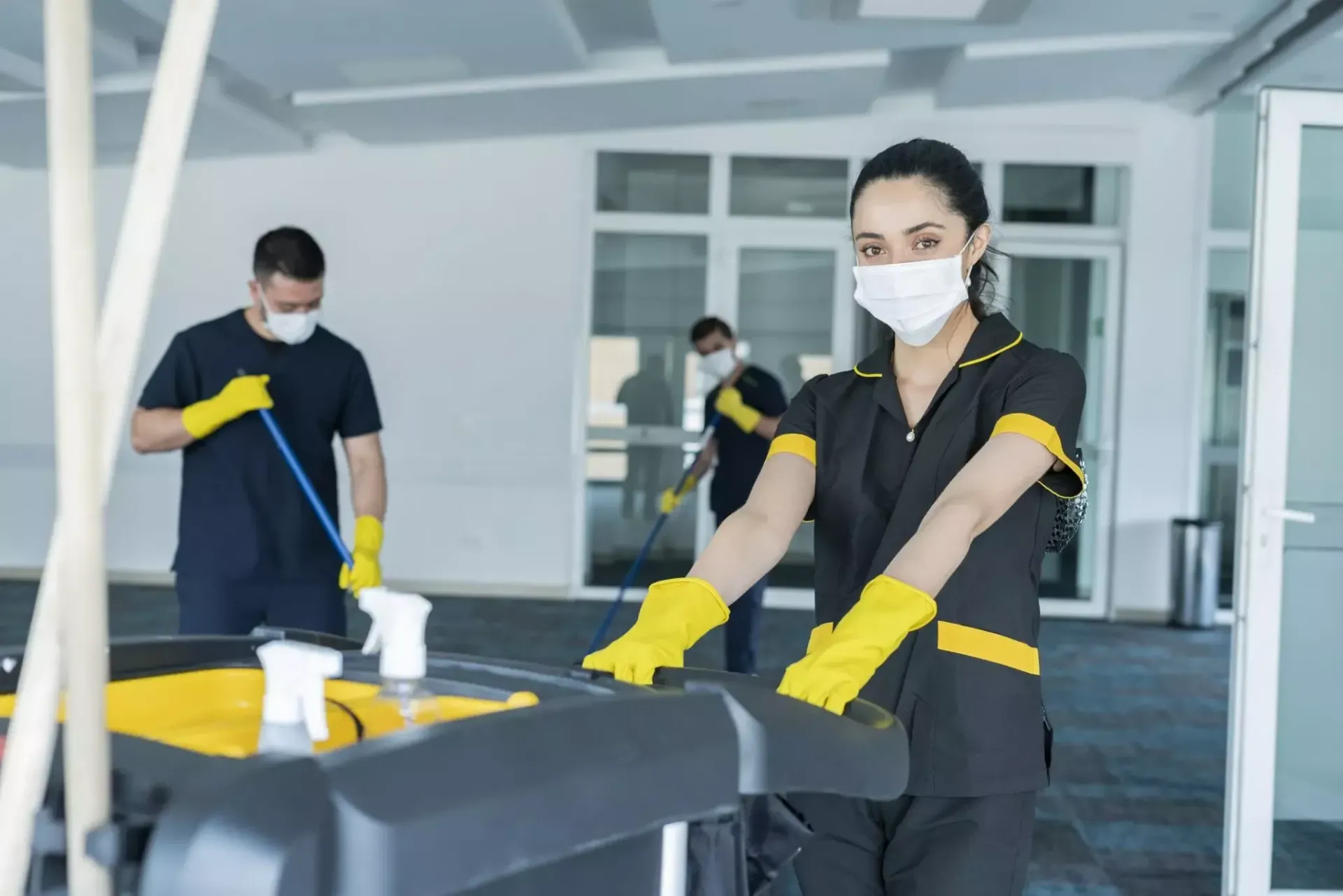 Two workers in yellow gloves cleaning an office floor with mops and a bucket