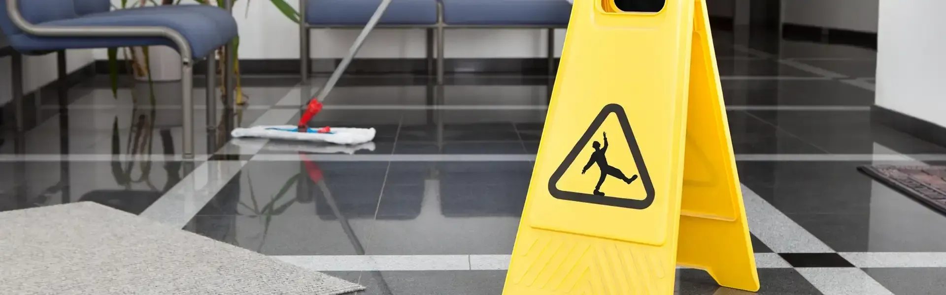 Yellow wet floor sign on a shiny tiled floor with a mop and bench in the background